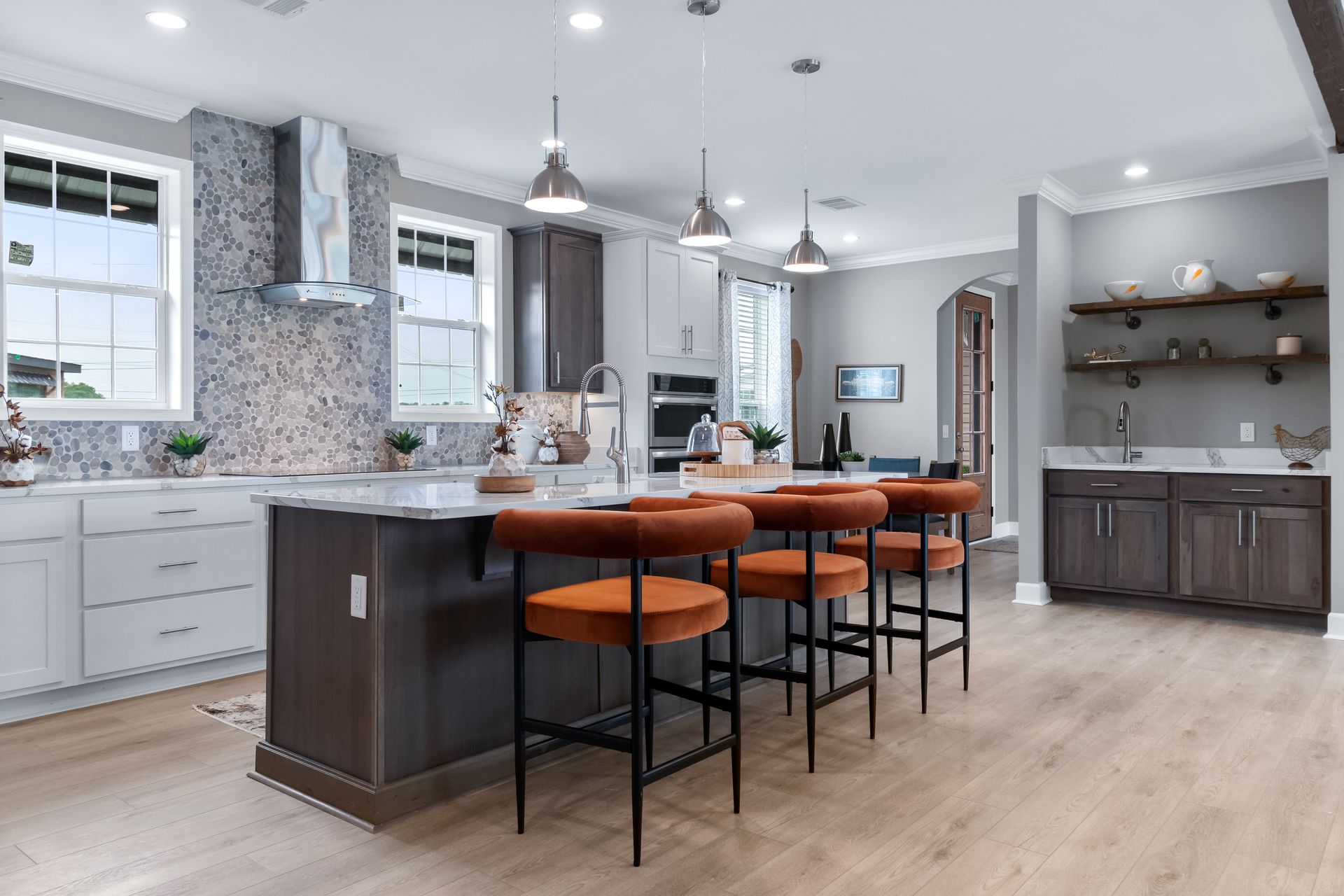 Modern kitchen with gray cabinets, large island, orange stools, and light wood flooring