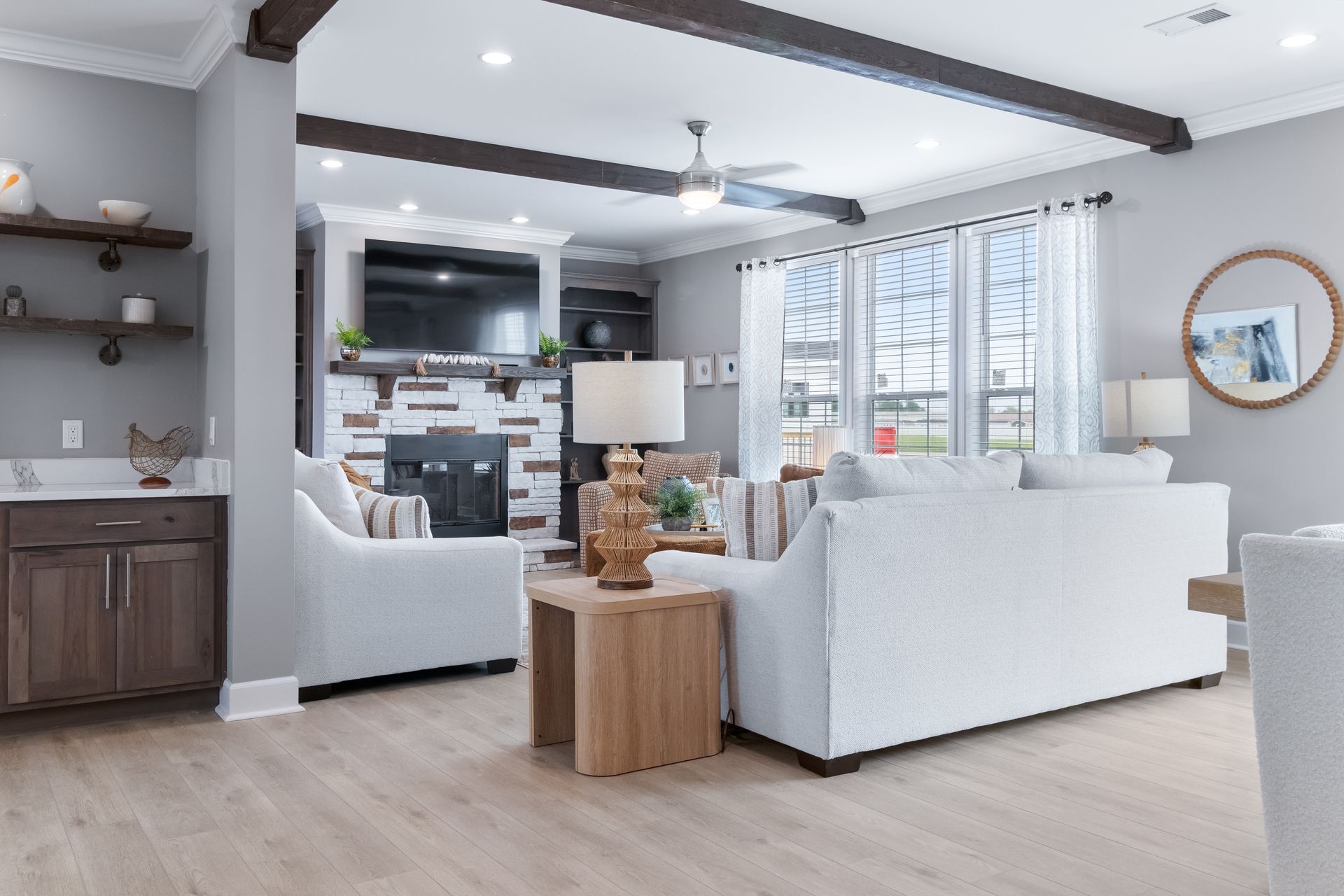 Modern open-concept living room with white sofas, wood accents, and large windows