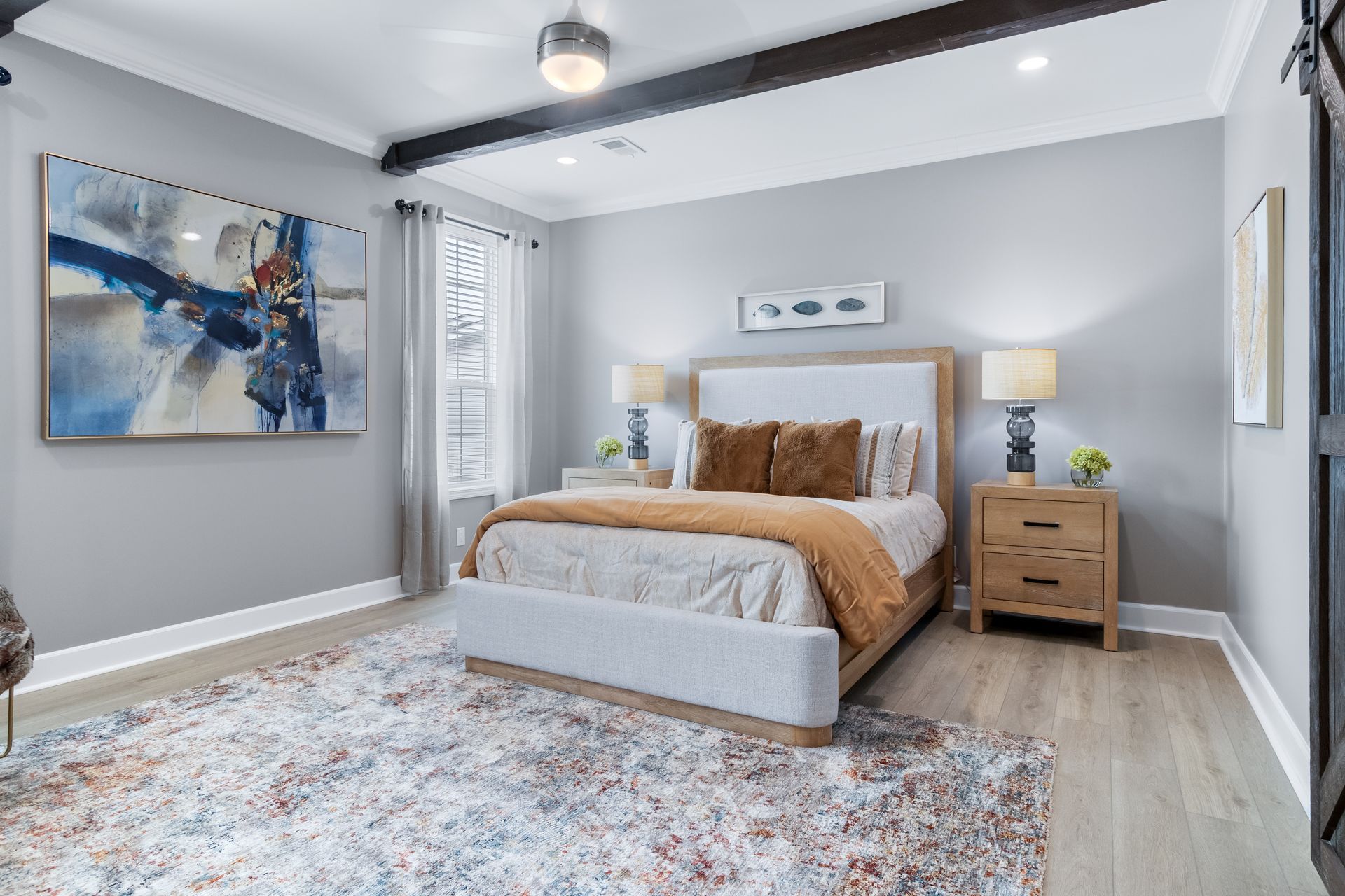 Modern gray bedroom with a bed, nightstands, abstract wall art, and a large patterned rug