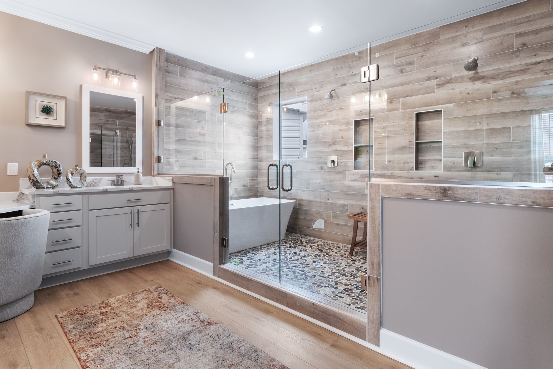 Modern bathroom with a glass-enclosed shower, vanity, and soaking tub in a light wood and stone design
