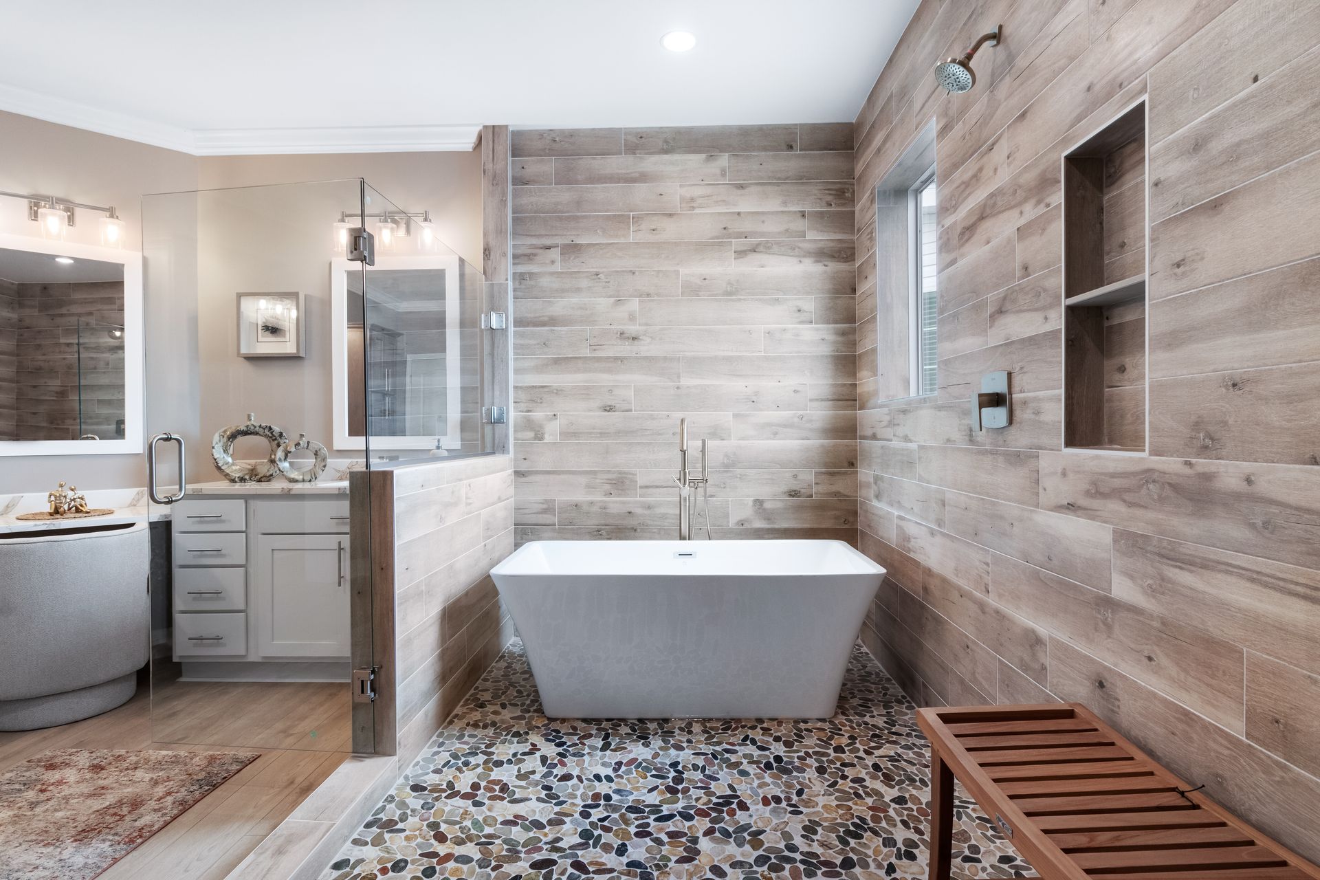 Modern bathroom with freestanding tub, wood-look tile walls, mosaic floor, and vanity sink.