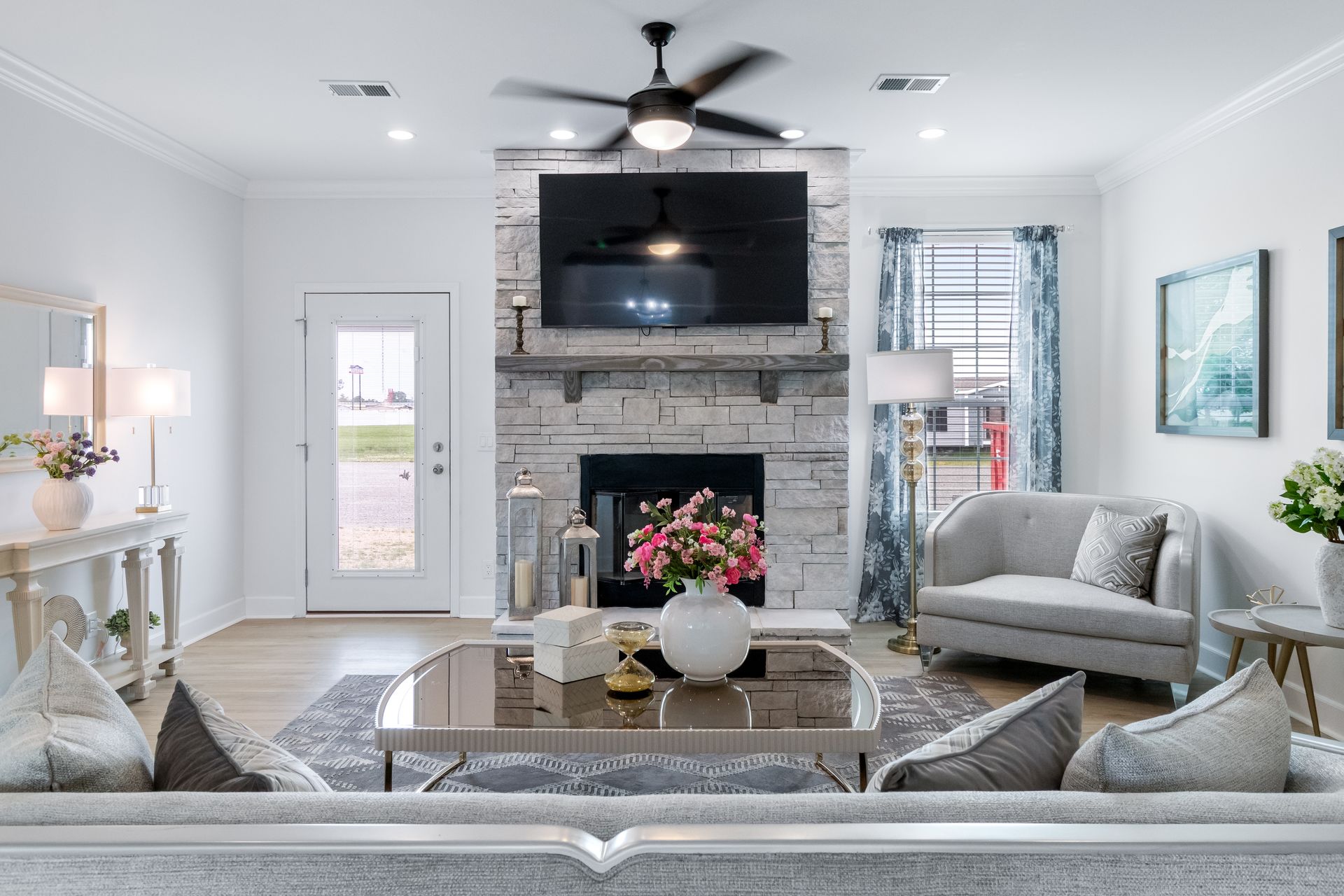 Bright living room with stone fireplace, large TV, gray sofas, coffee table, and light blue accents