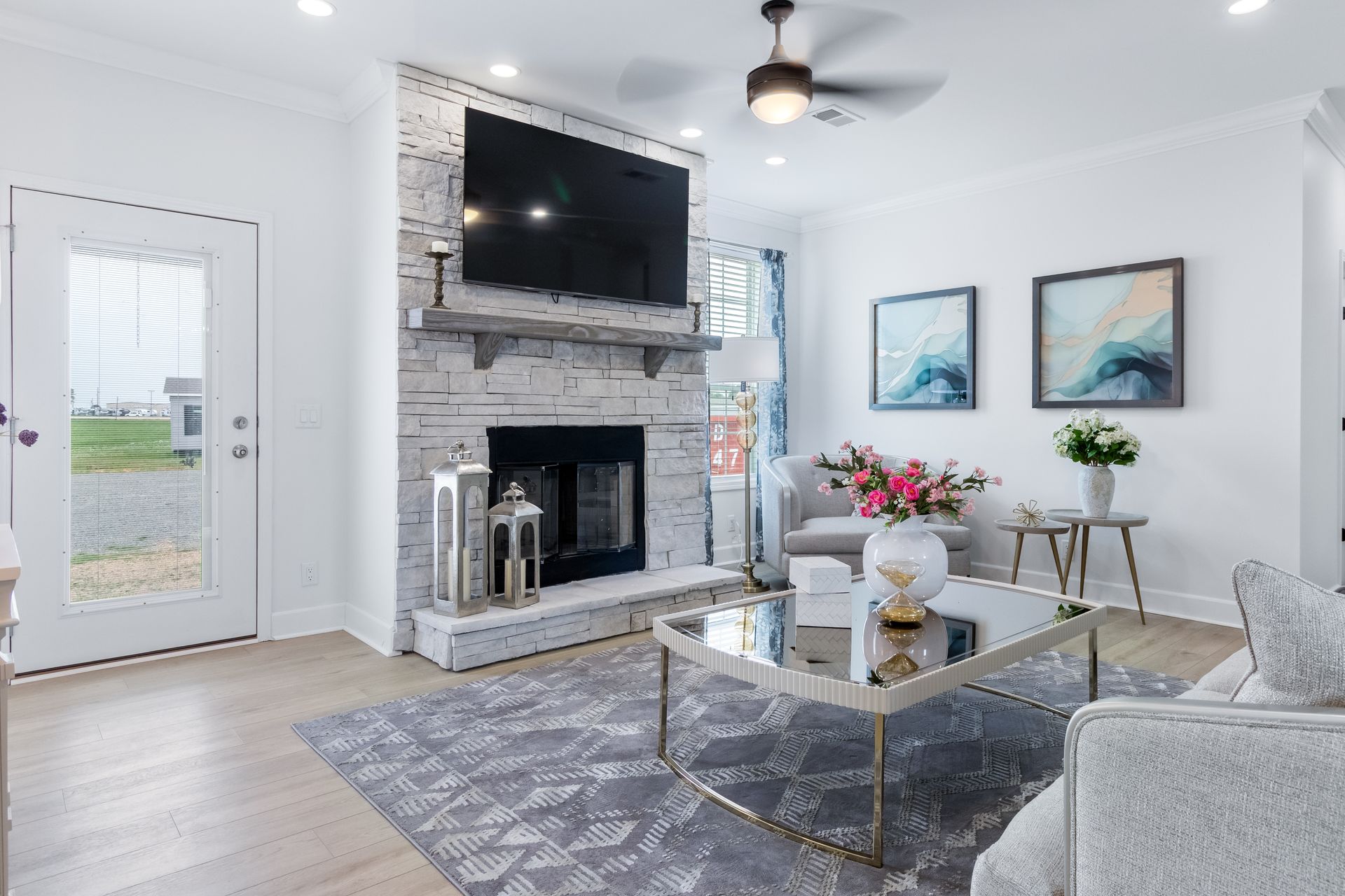 Bright living room with a stone fireplace, TV, glass coffee table, and white decor