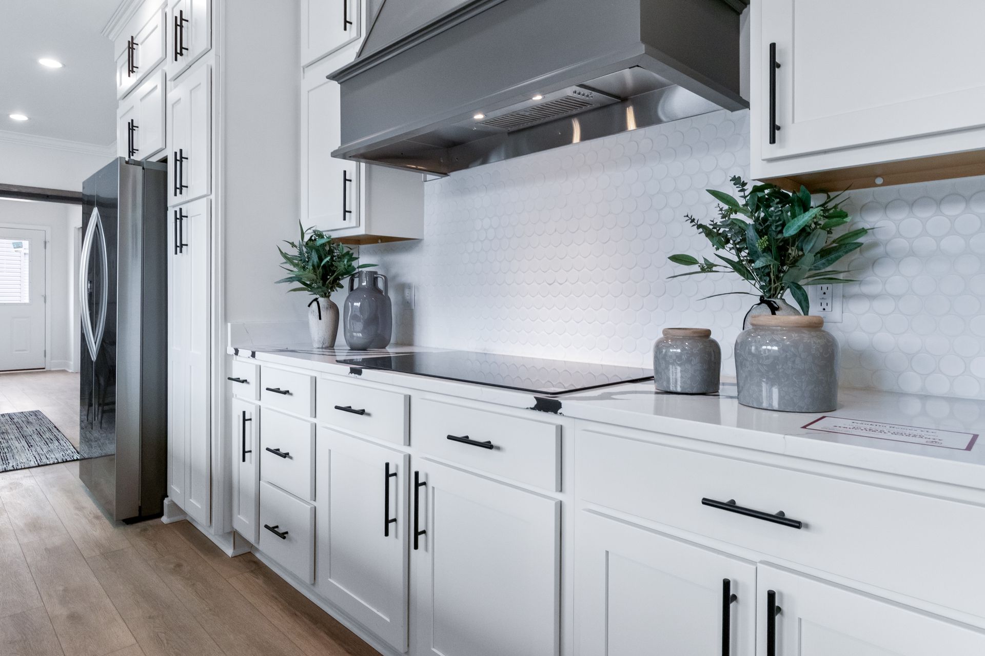 Modern white kitchen with stainless steel appliances, tiled backsplash, and potted plants on the counter
