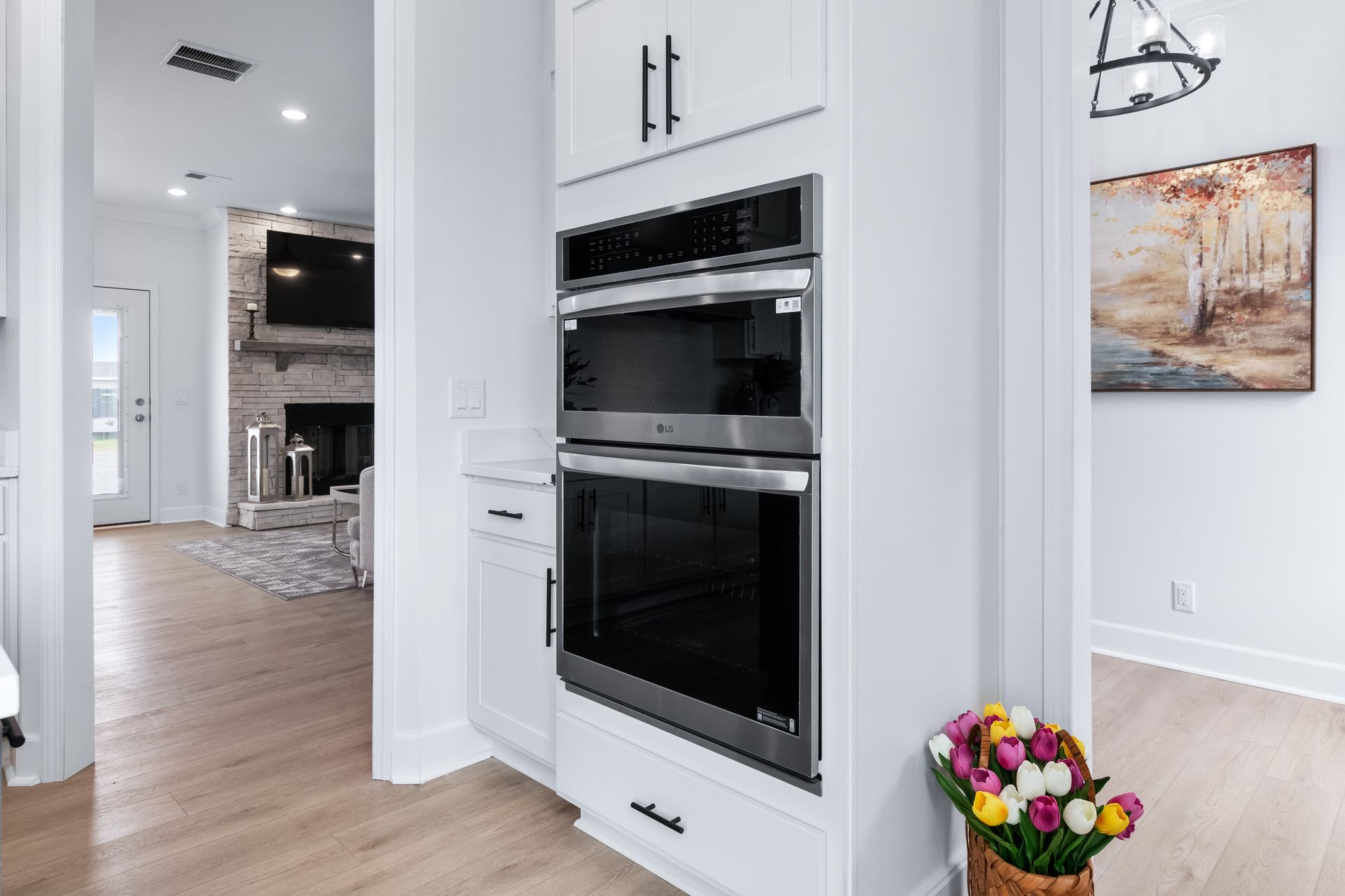 Bright modern kitchen with white cabinets, double ovens, hardwood floor, and flowers by the wall.