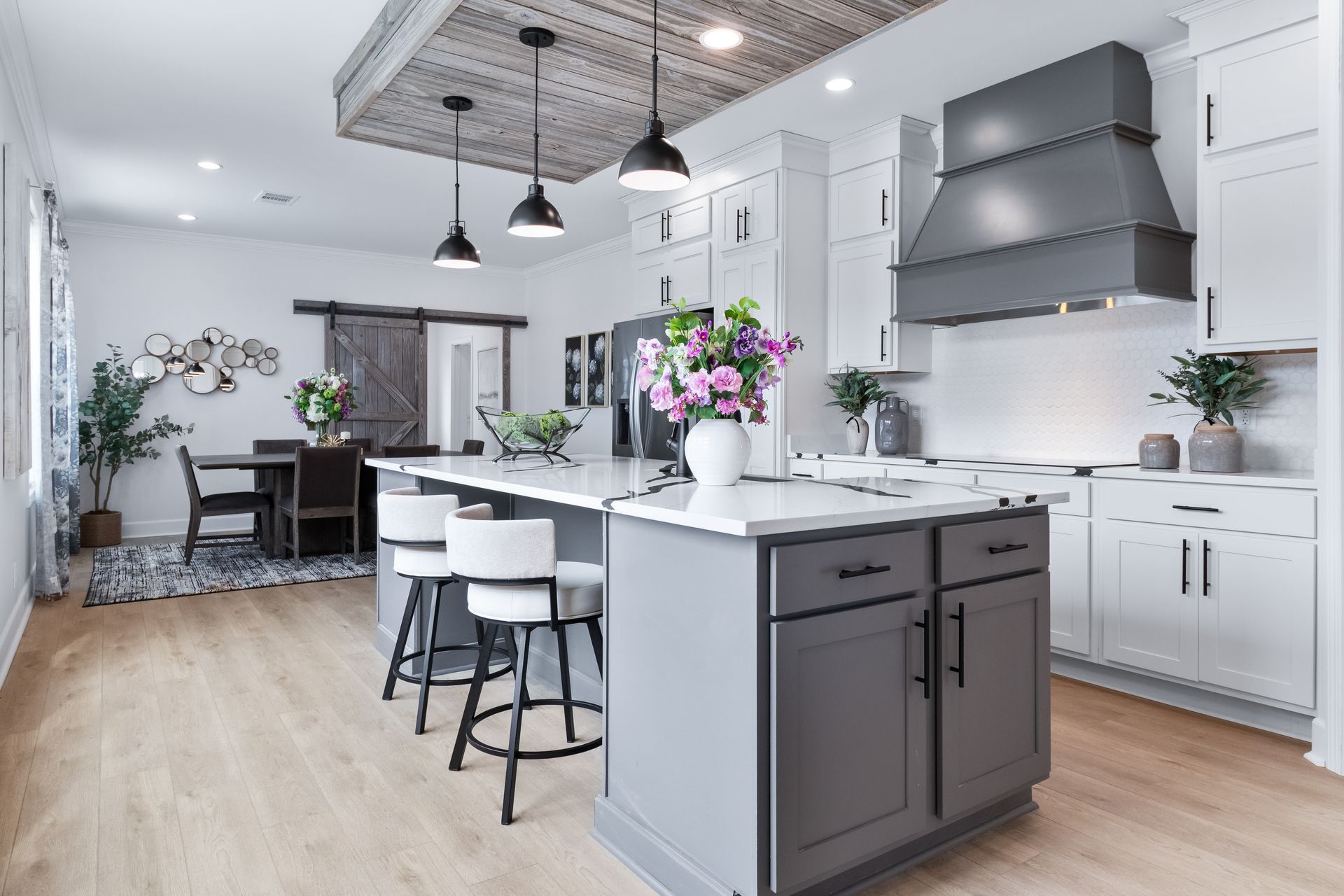 Modern white kitchen with island, barstools, pendant lights, and stainless range hood
