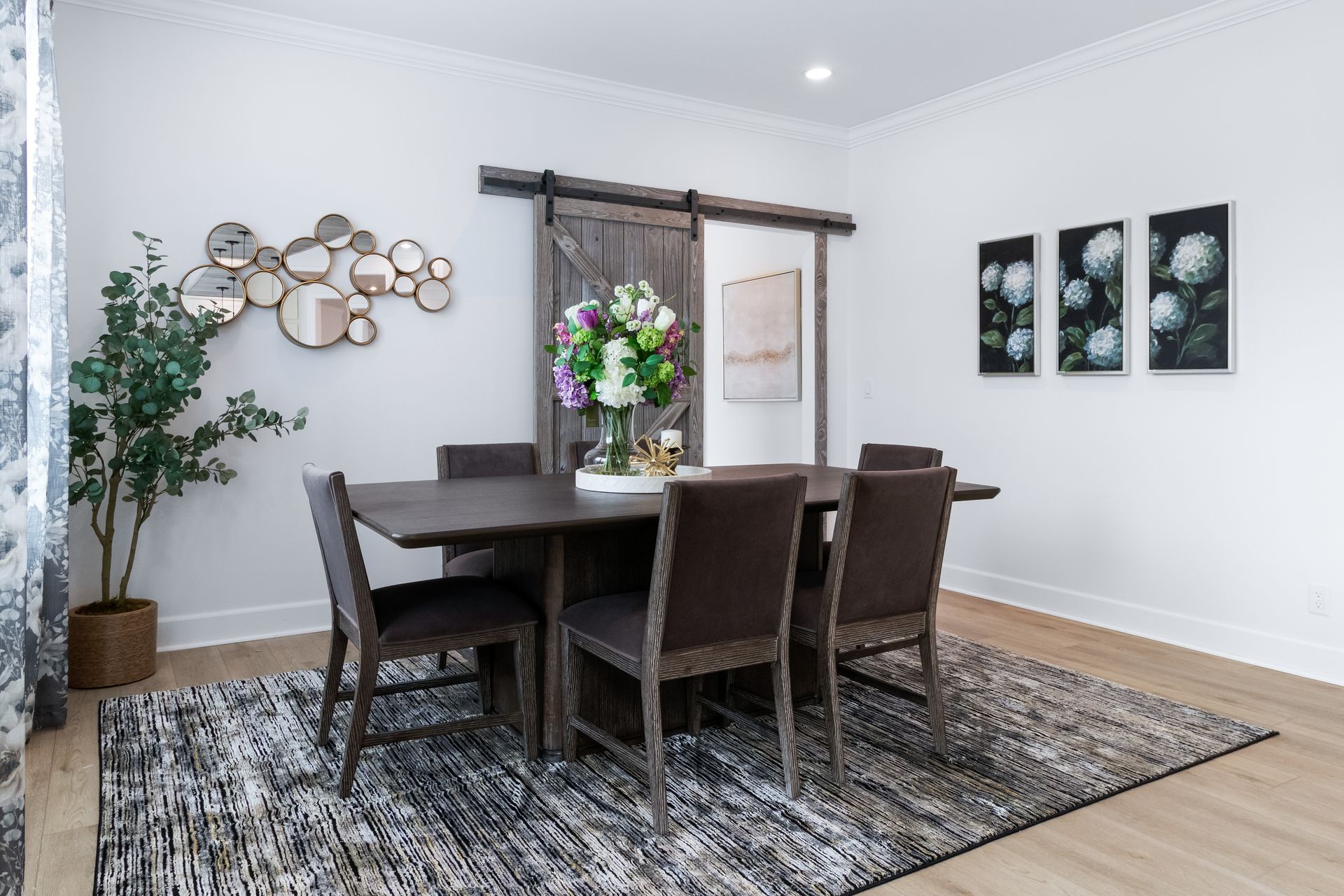 Modern dining room with dark wood table, chairs, patterned rug, and wall art in a bright space