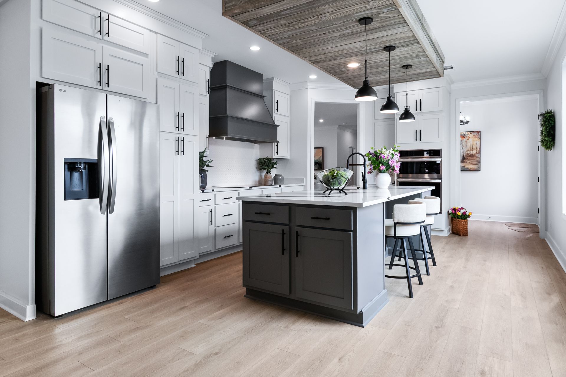 Modern white kitchen with stainless steel fridge, dark island, pendant lights, and light wood floors