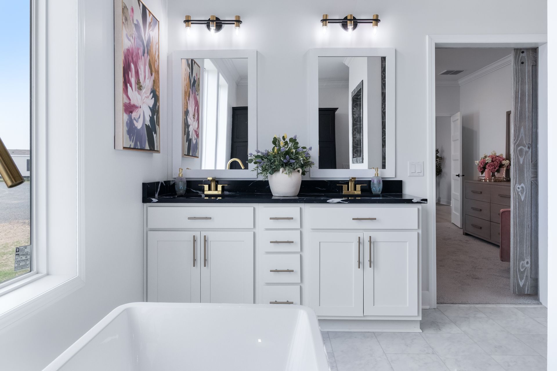 Modern bathroom vanity with double mirrors, black countertop, white cabinets, and a freestanding tub edge visible