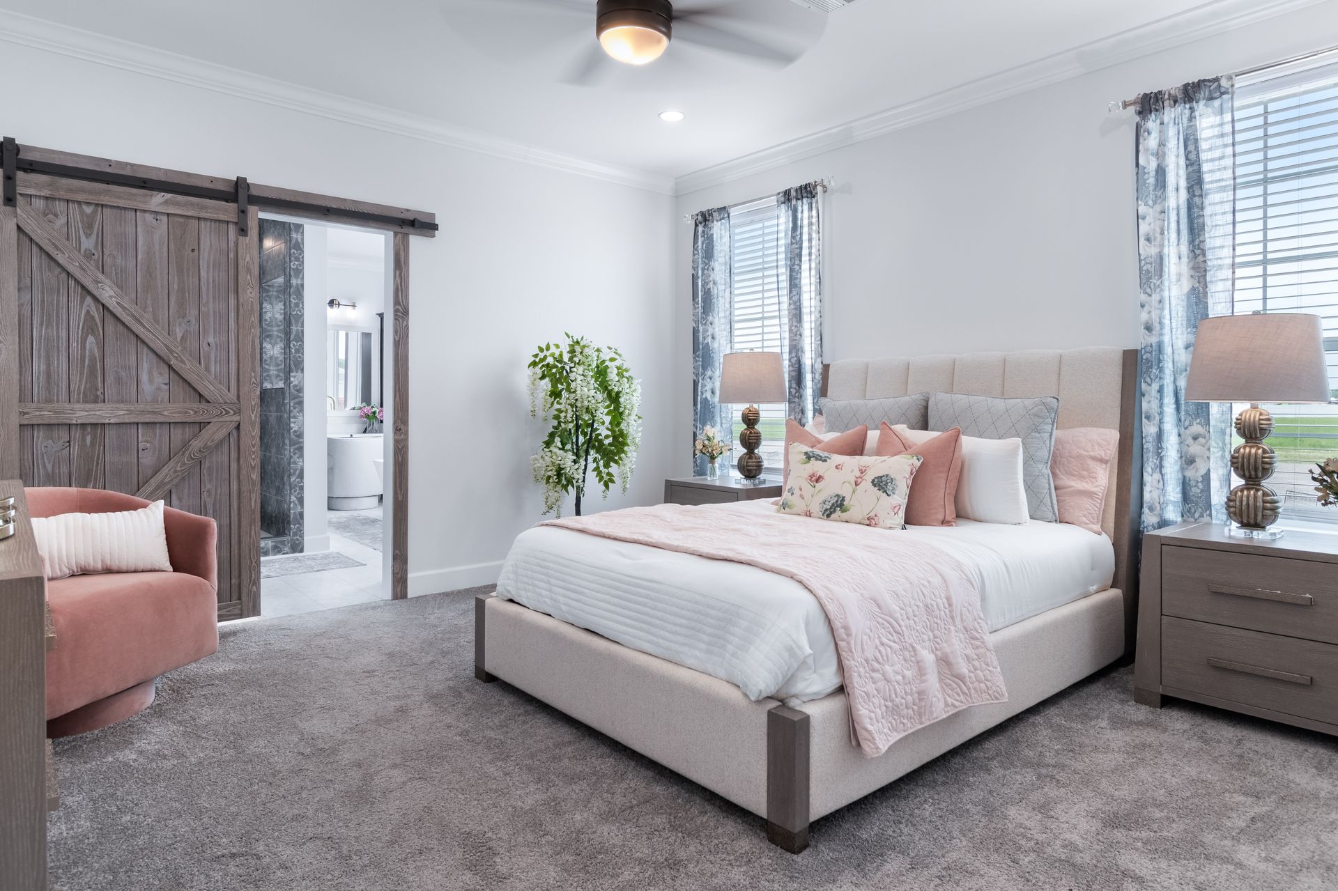 Bright bedroom with gray carpet, a white upholstered bed, pink accents, and wooden sliding barn doors.