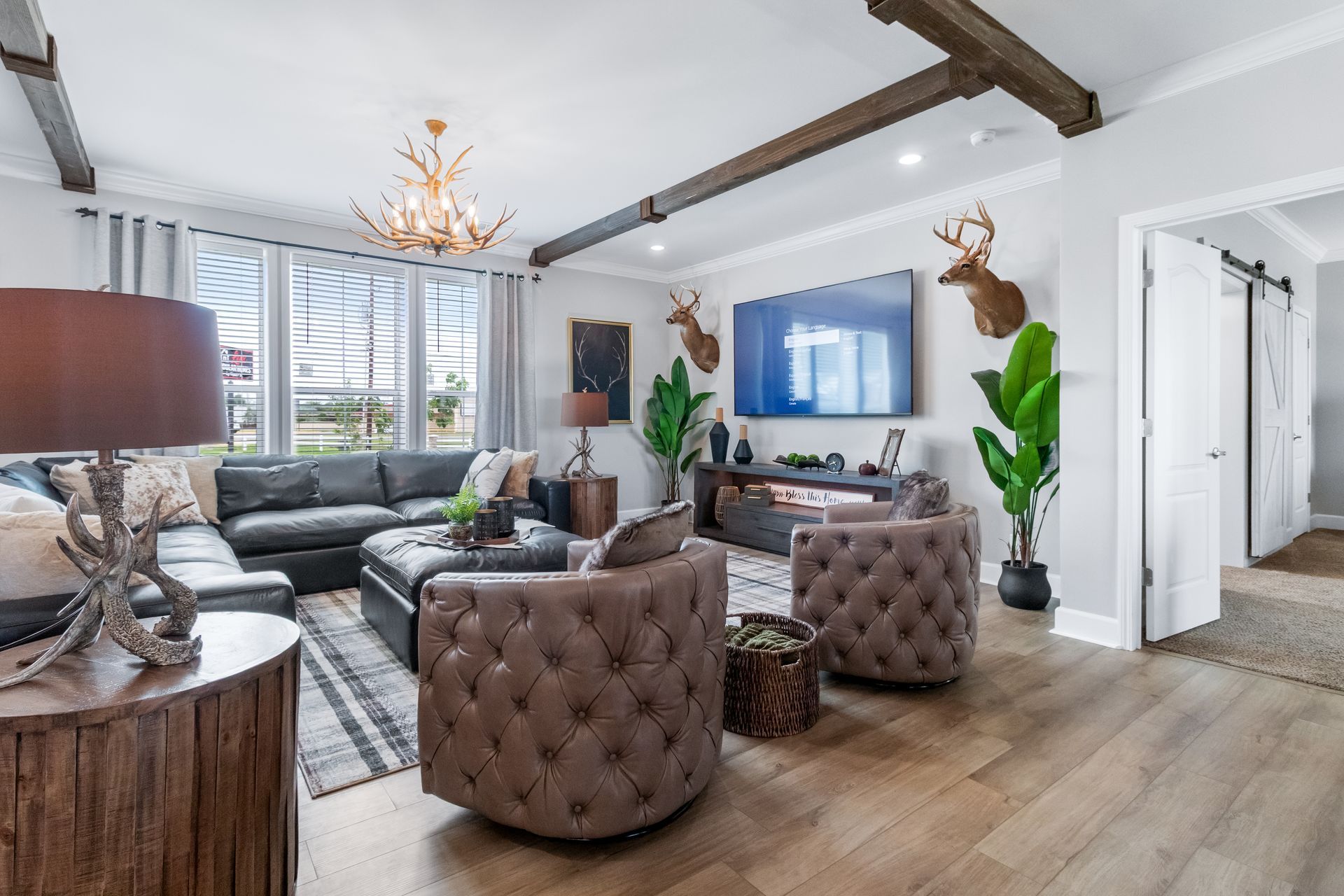 Bright living room with gray sectional, tufted chairs, fireplace, TV, wood beams, and large windows