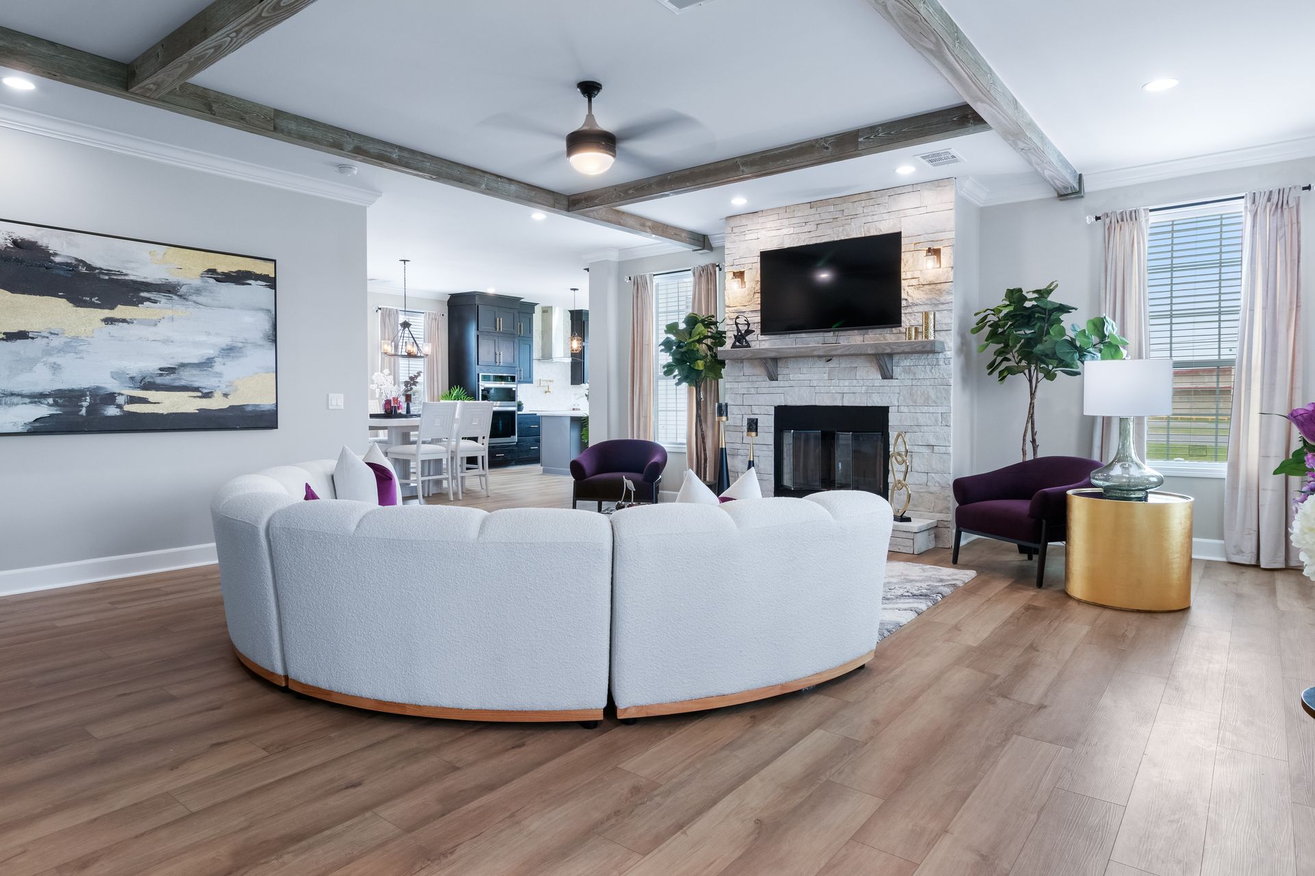 Bright modern living room with curved white sofa, fireplace, wall-mounted TV, and wood floors.