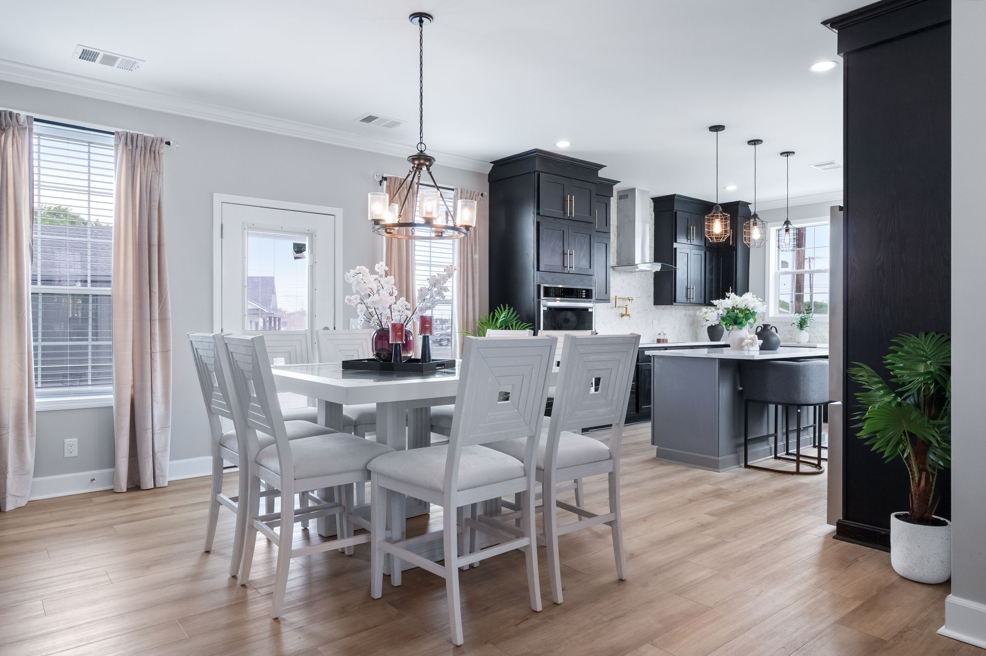 Bright open dining and kitchen area with white chairs, dark cabinets, and light wood floors