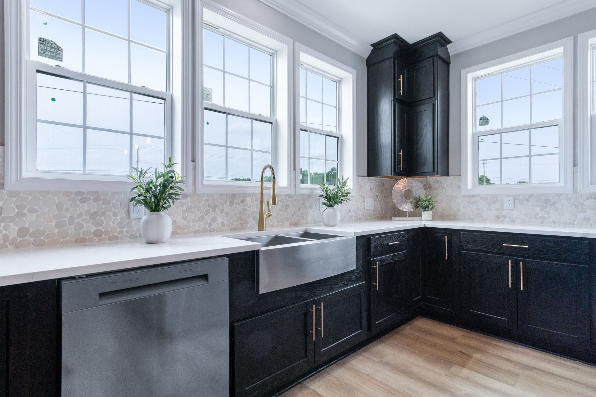 Bright kitchen with black cabinets, white countertops, large windows, and a farmhouse sink