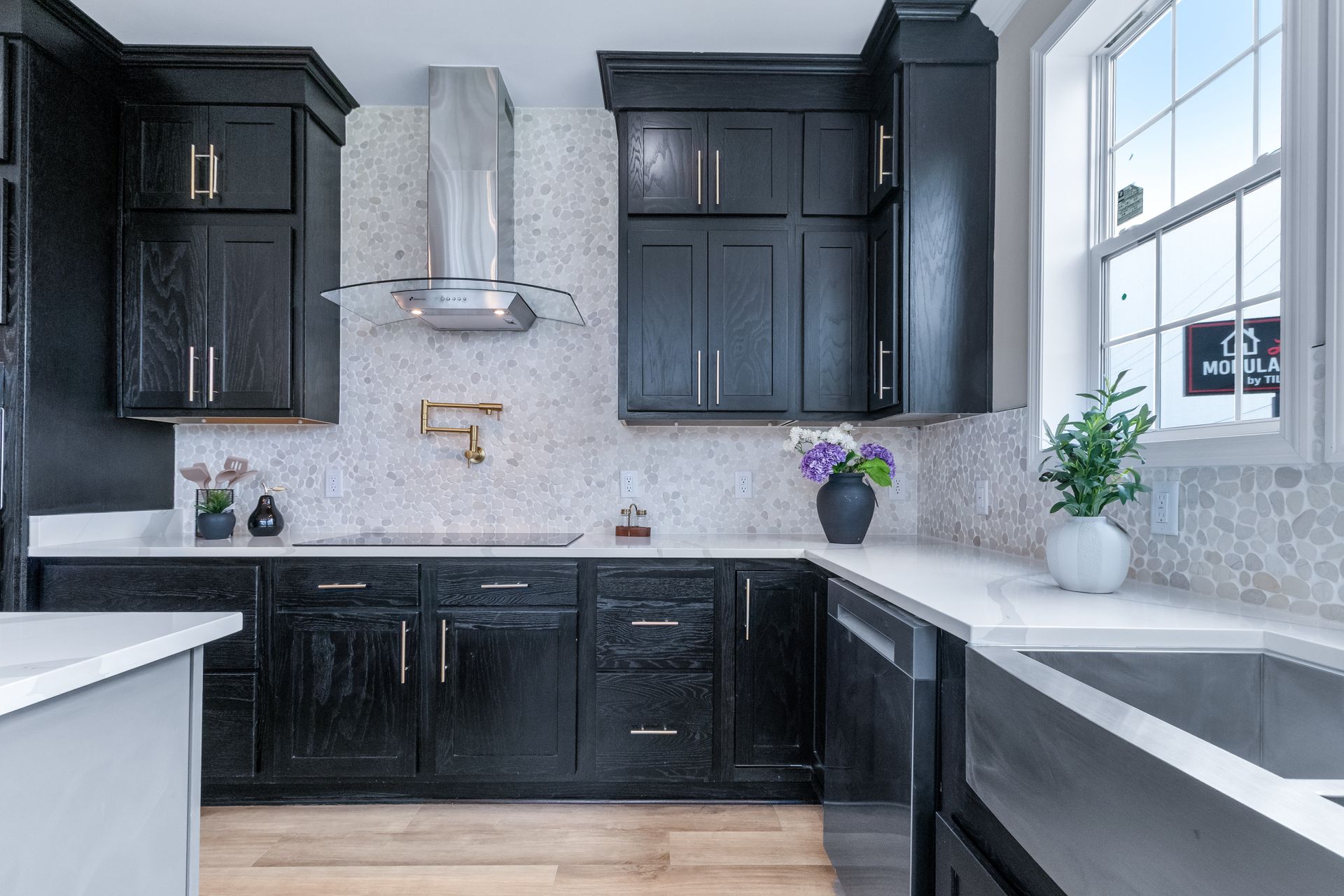 Modern black-and-white kitchen with dark cabinets, marble-look backsplash, and stainless range hood