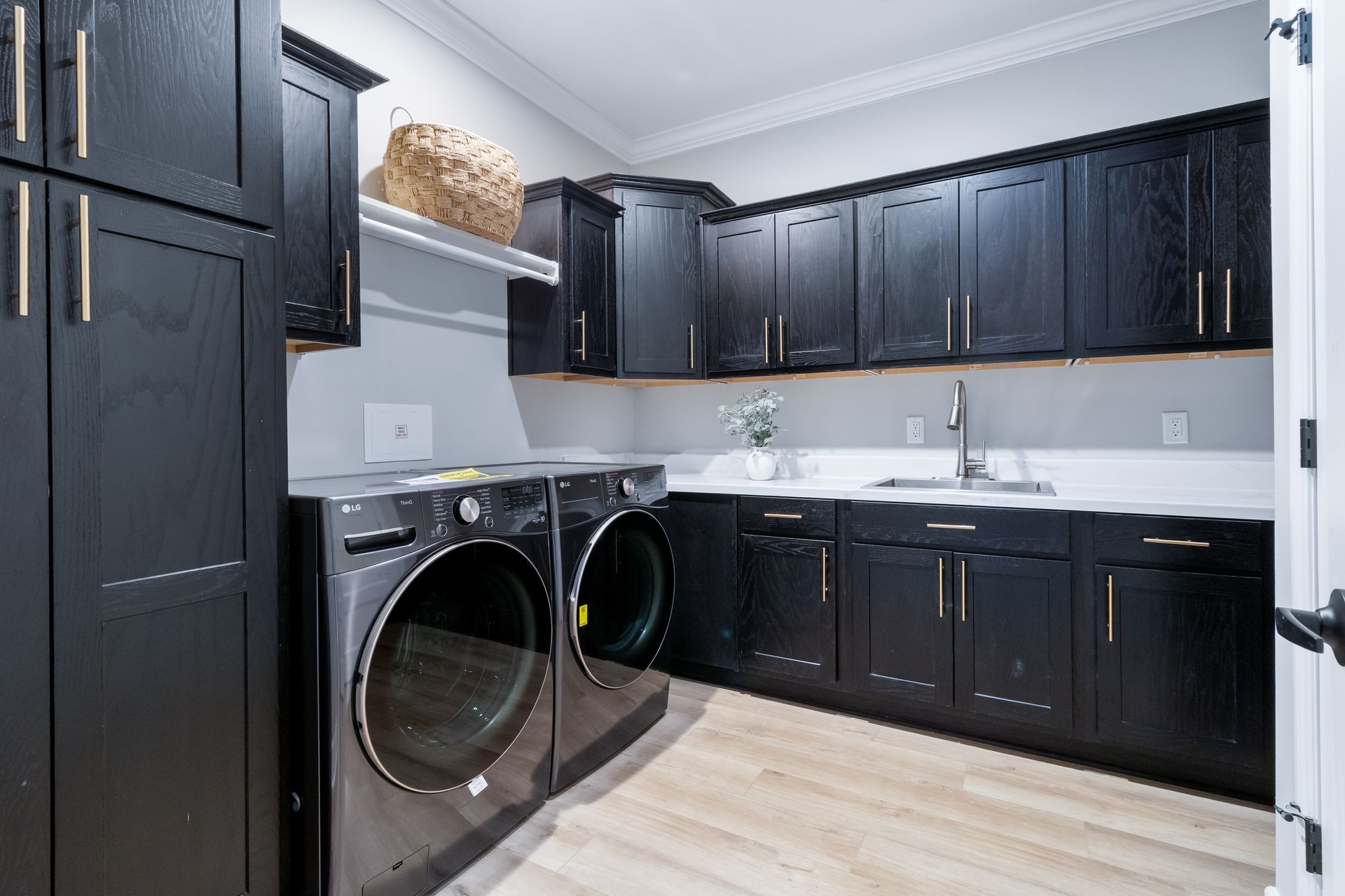 Black laundry room with front-loading washer and dryer, dark cabinets, white countertop, and light wood floor