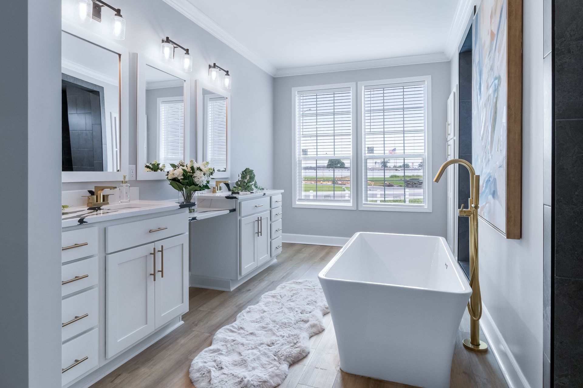 Bright white bathroom with freestanding tub, double vanity, and large window overlooking a lawn.