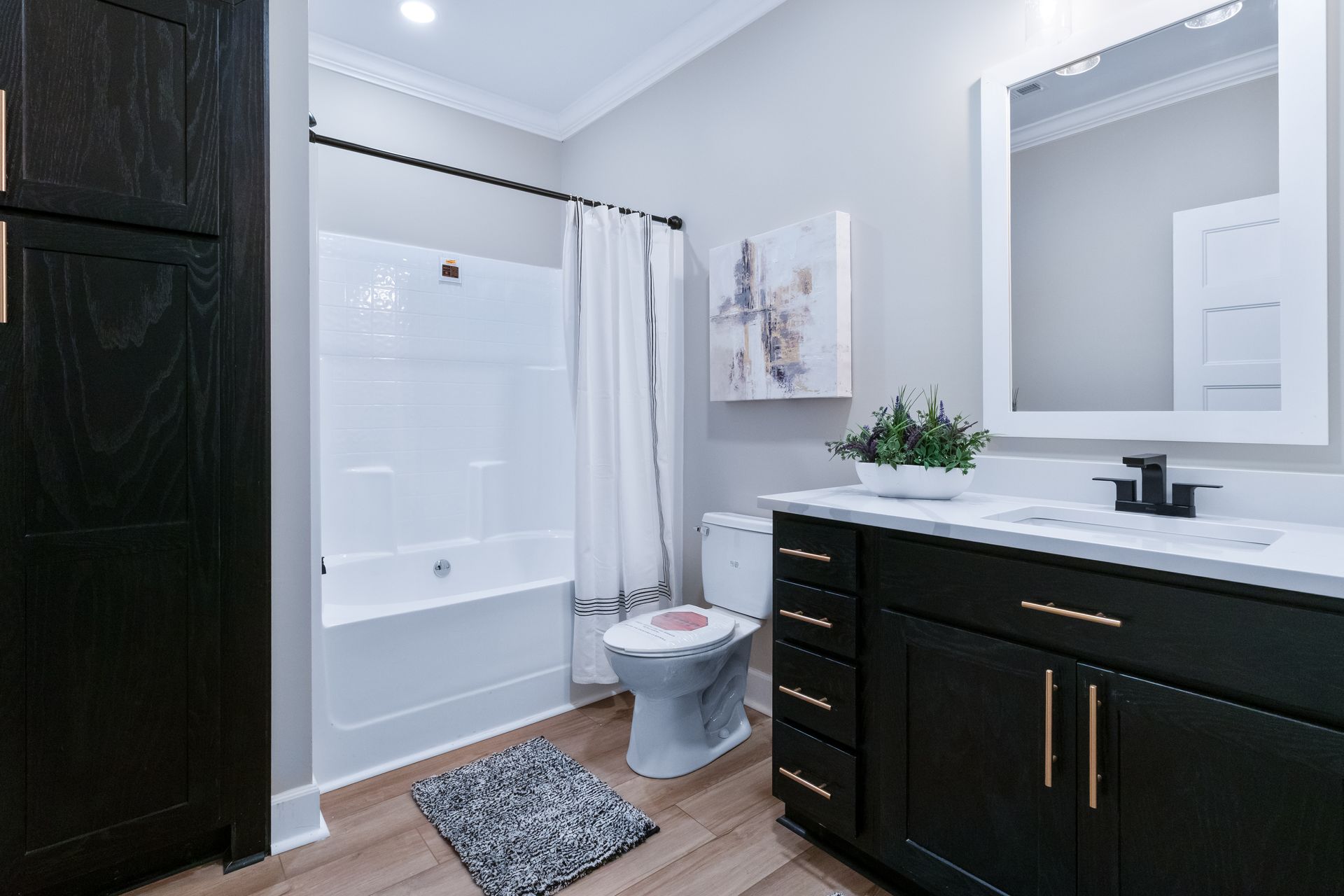 Modern bathroom with dark vanity, white tub shower, toilet, and large mirror