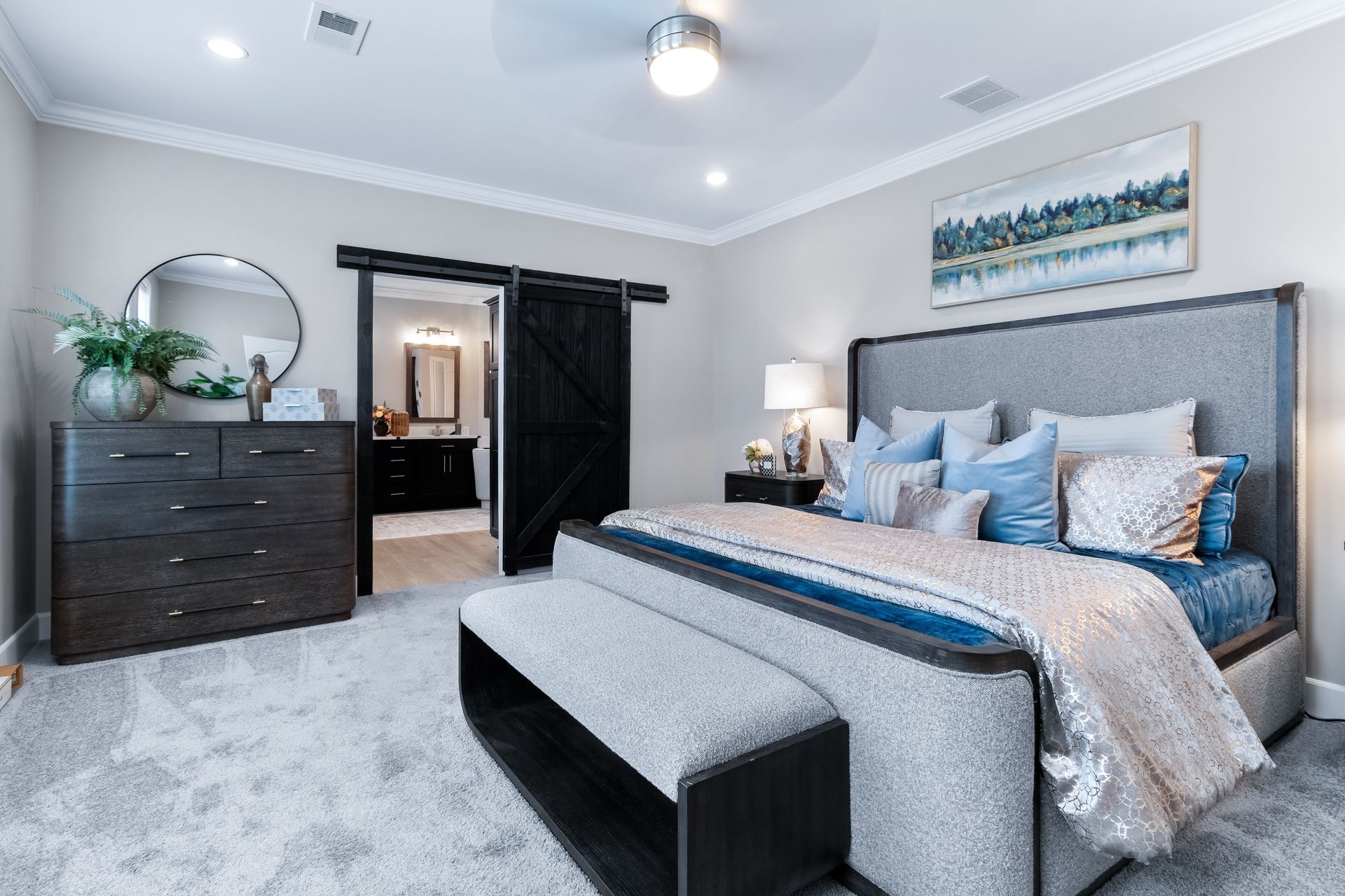 Bright gray bedroom with a large upholstered bed, dark dresser, mirrored doors, and blue accent decor.