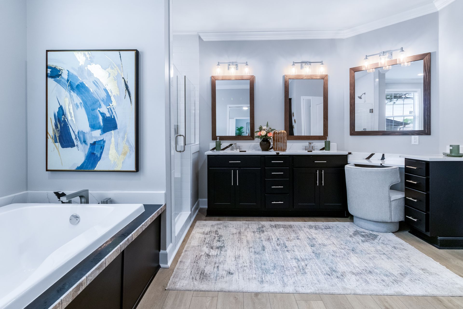 Modern bathroom with double vanity, framed mirrors, tub, and blue abstract wall art