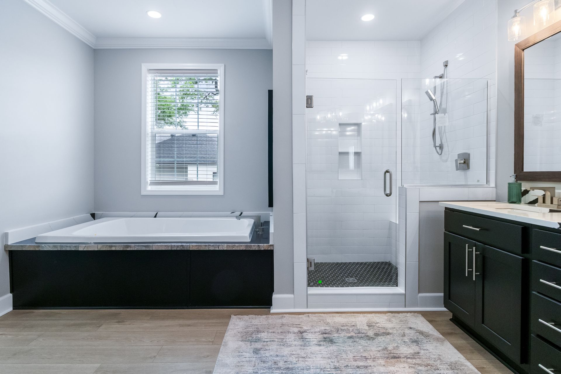 Modern bathroom with a black soaking tub, glass shower, and dark vanity under a window.