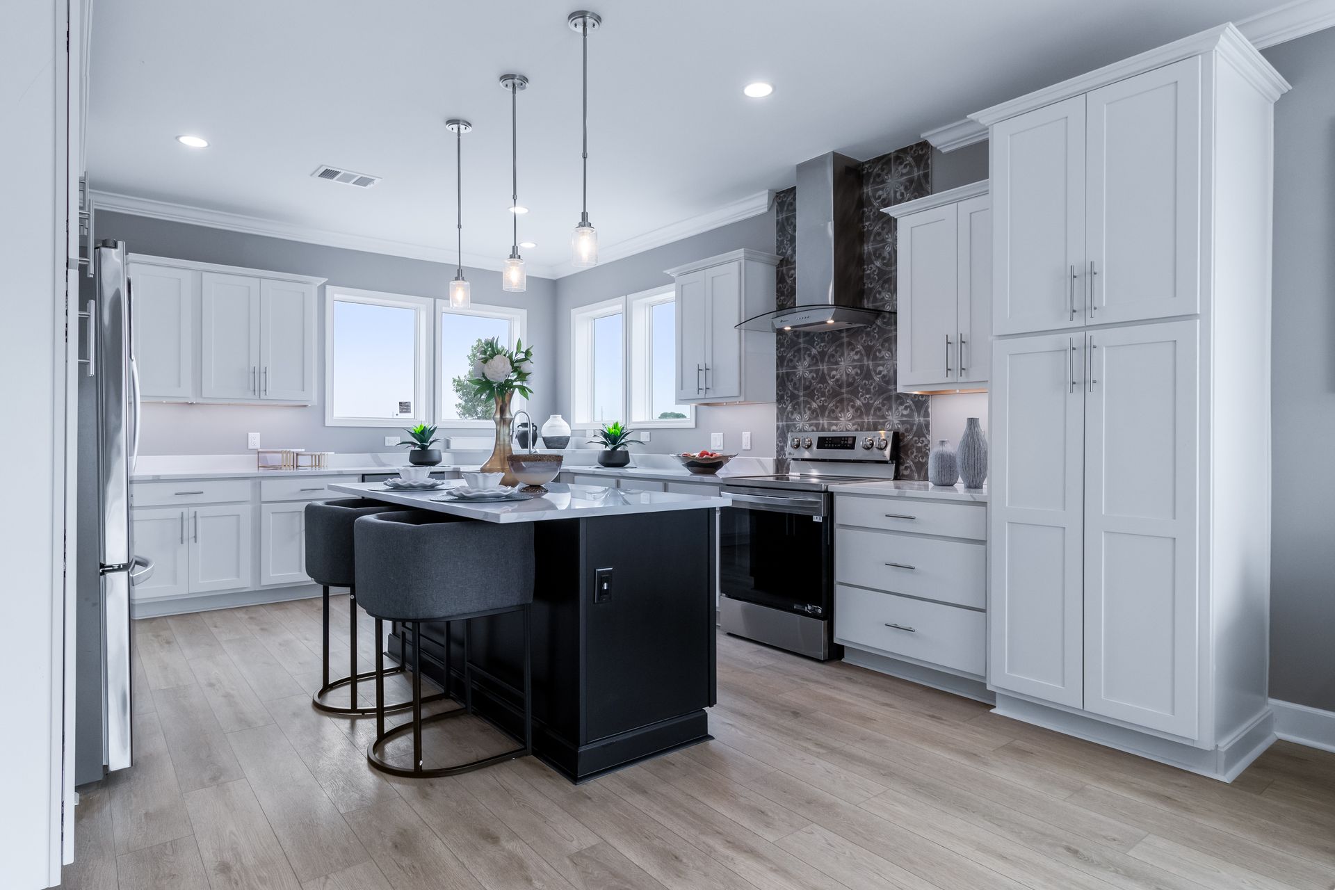 Bright modern kitchen with white cabinets, black island, pendant lights, and gray backsplash.