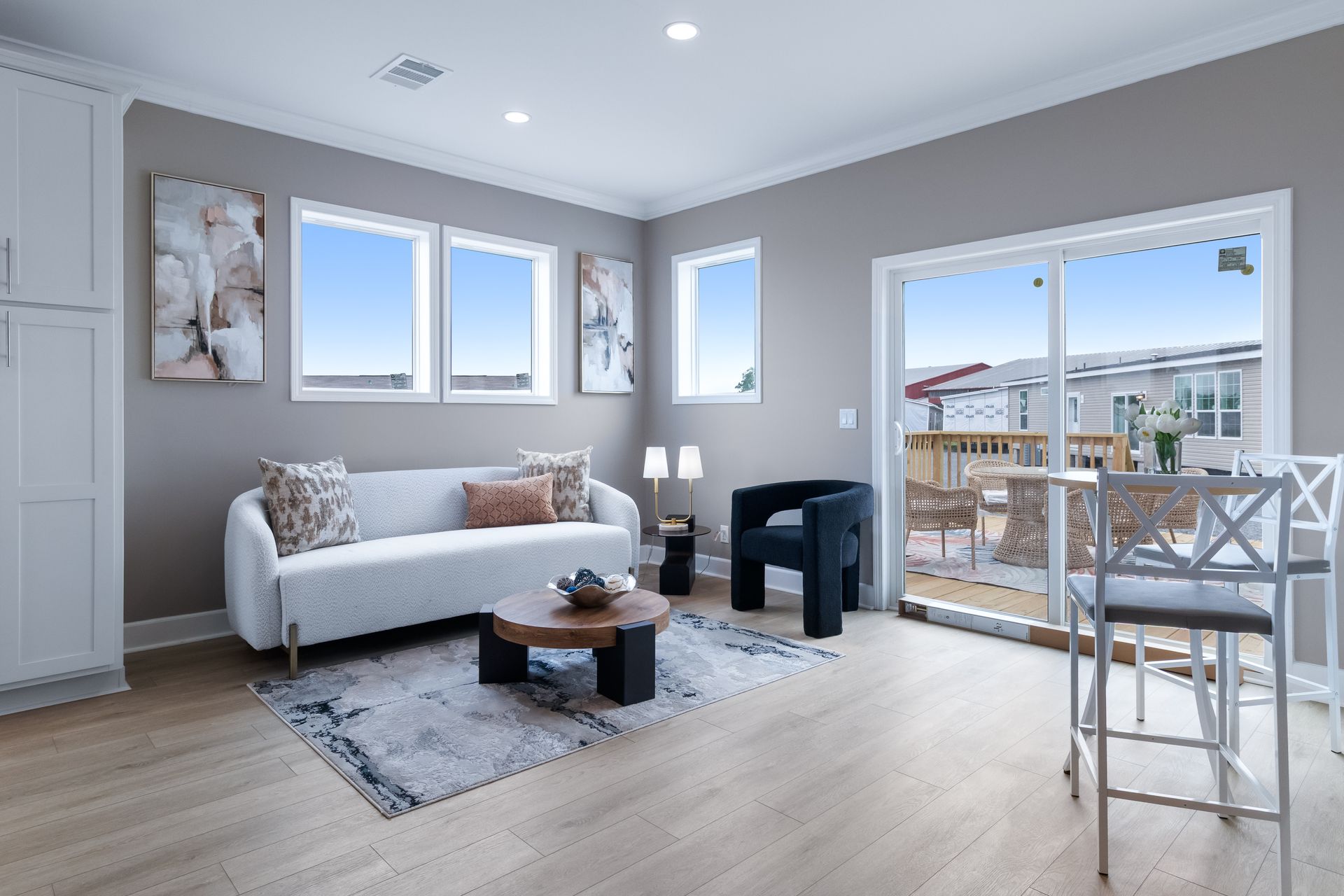 Bright modern living room with white sofa, gray rug, balcony door, and small dining table