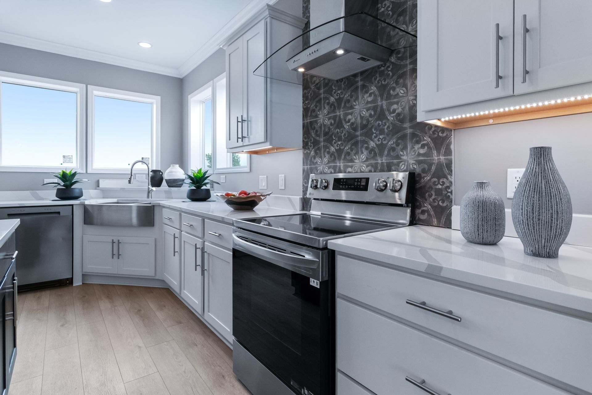 Bright modern kitchen with white cabinets, black stove, gray tile backsplash, and a large window over the sink