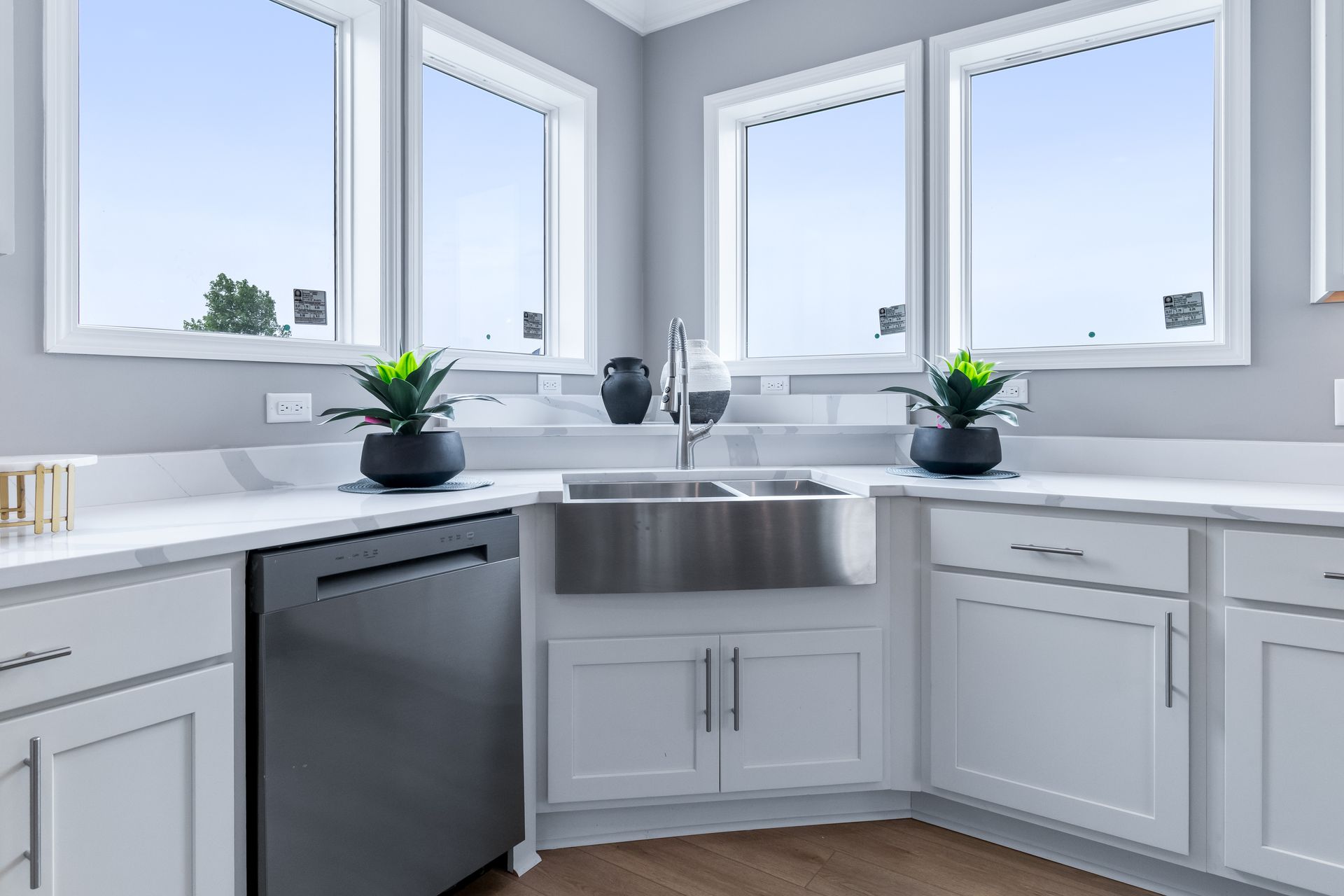 Bright modern kitchen sink area with white cabinets, stainless sink, and large windows.