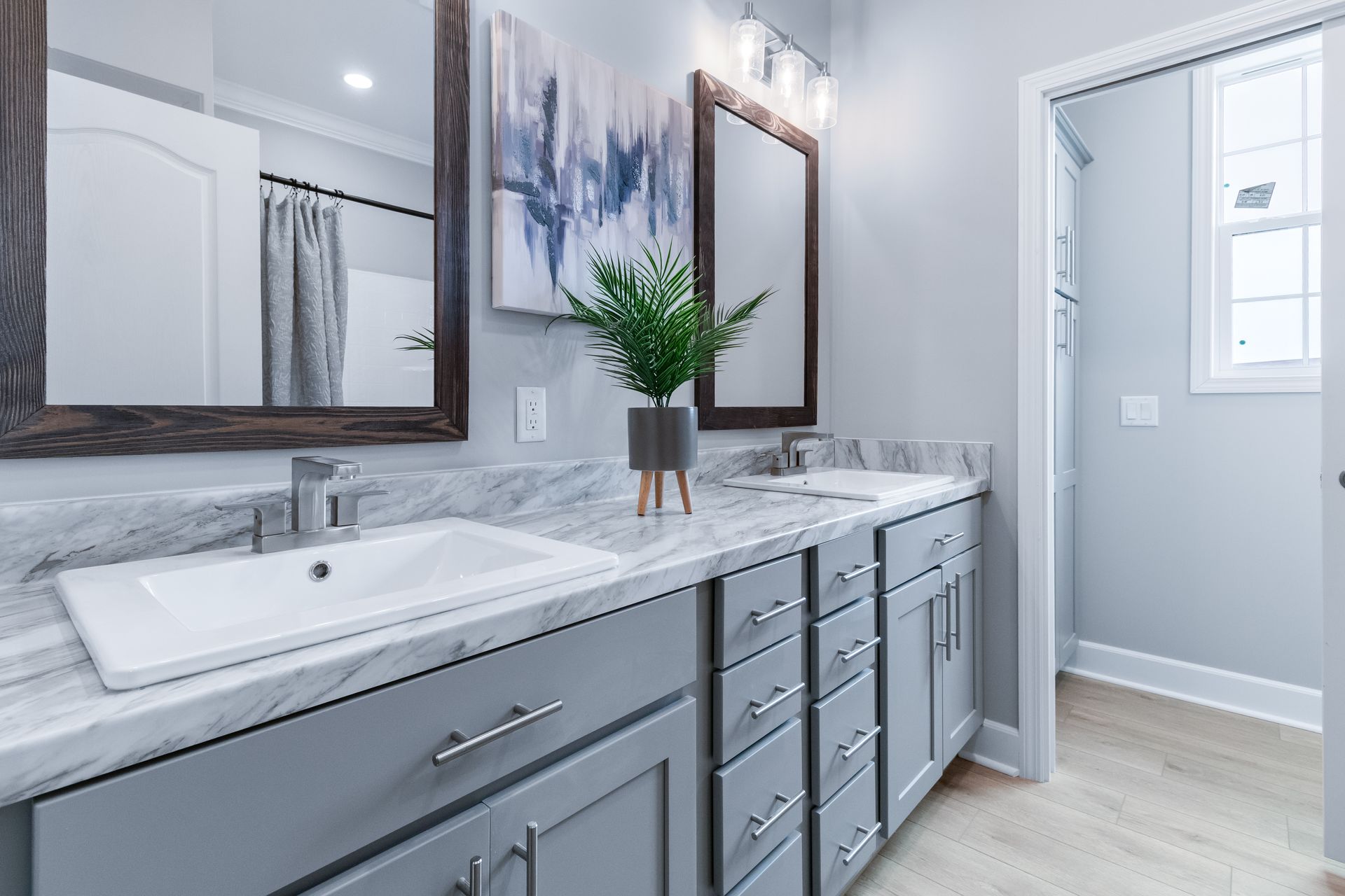 Modern bathroom vanity with double sinks, gray cabinets, mirrors, and a vase of greenery