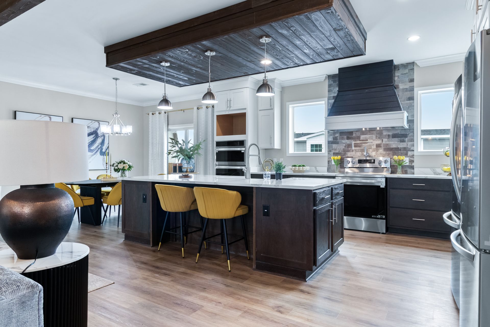 Modern kitchen with dark island, yellow stools, wood ceiling, and stainless steel appliances
