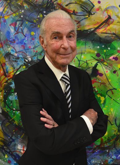 Woman with dark hair smiles, wearing a black top and jewelry, poses against a white backdrop.
