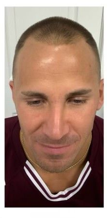 Man with short hair looking down, wearing a maroon shirt with white trim, gold chain.