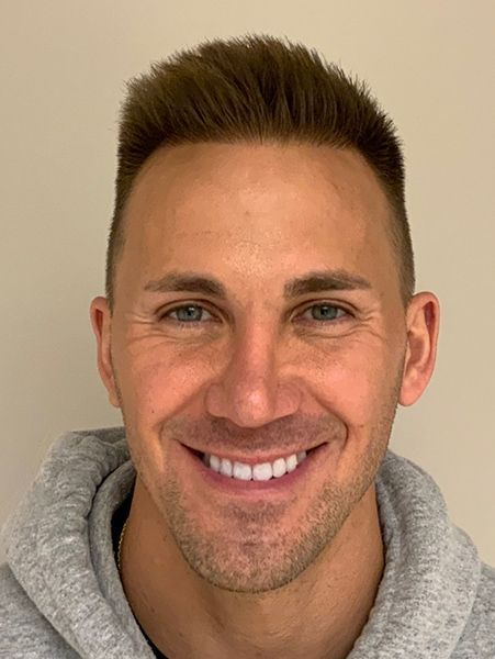 Man with short, light brown hair and a gray hoodie smiles at the camera.