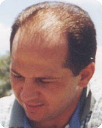Man with thinning brown hair, looking down, outdoors.