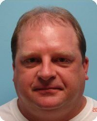 Man with short brown hair and a neutral expression, against a light blue background.