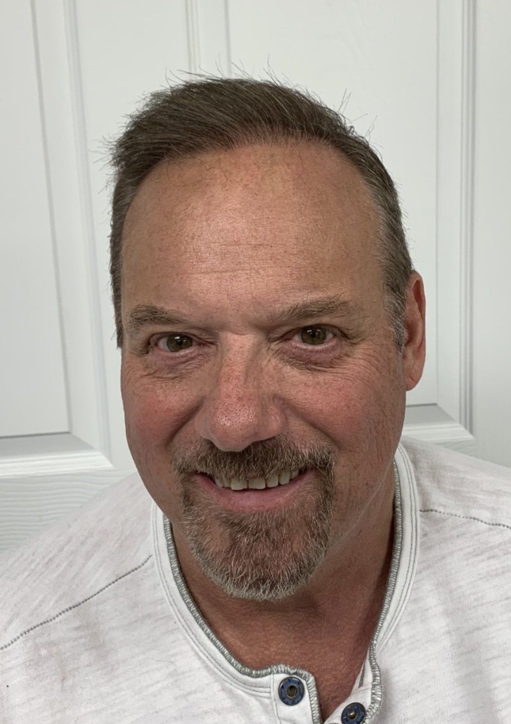 Man with short brown hair and beard smiles, wearing a light colored shirt.