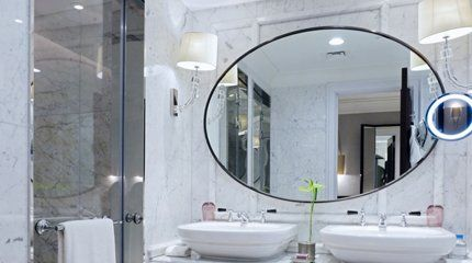 Luxurious bathroom with marble walls, oval mirror, and double sinks.