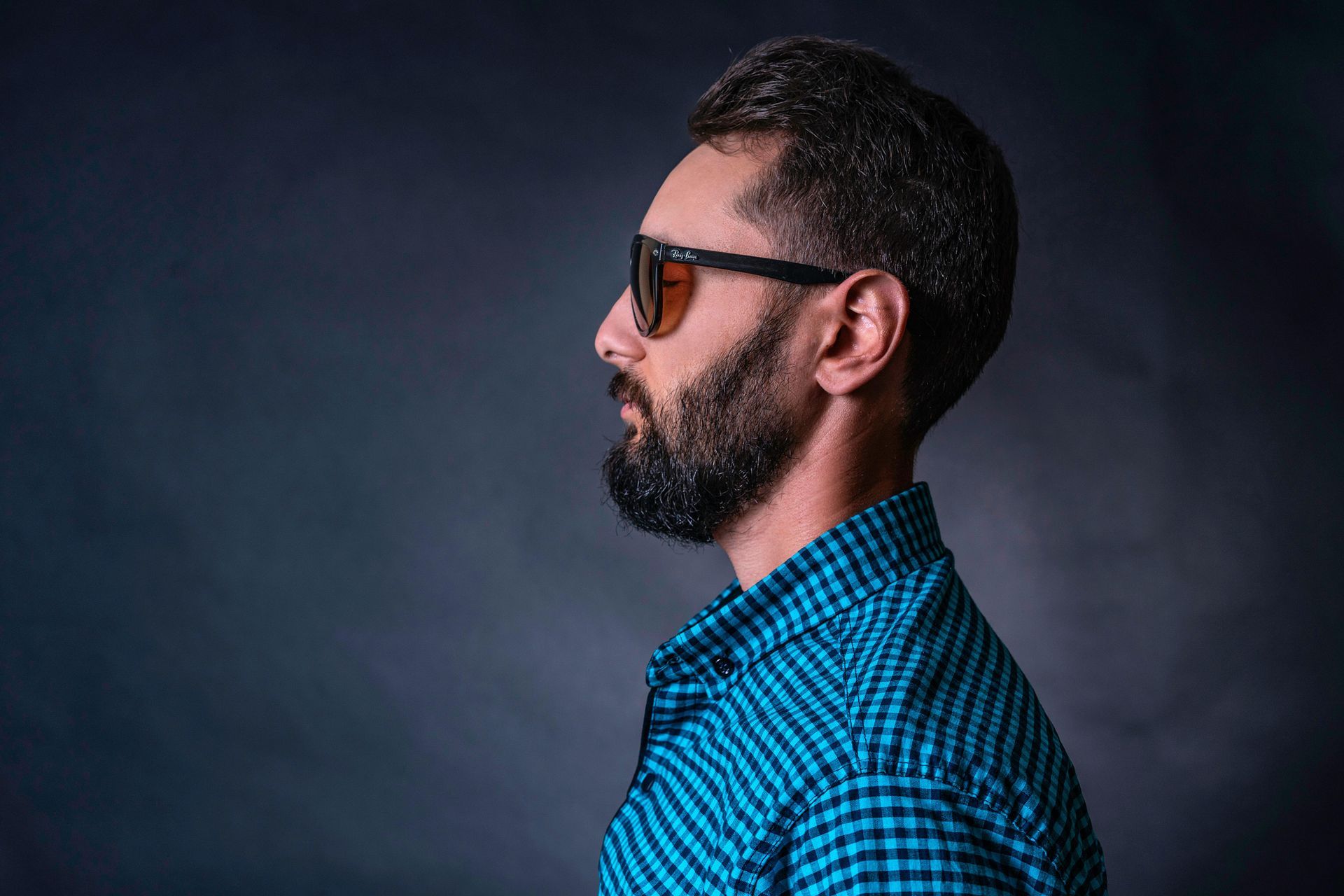 Man in black shirt adjusting cuff, looking to the side against a dark background.