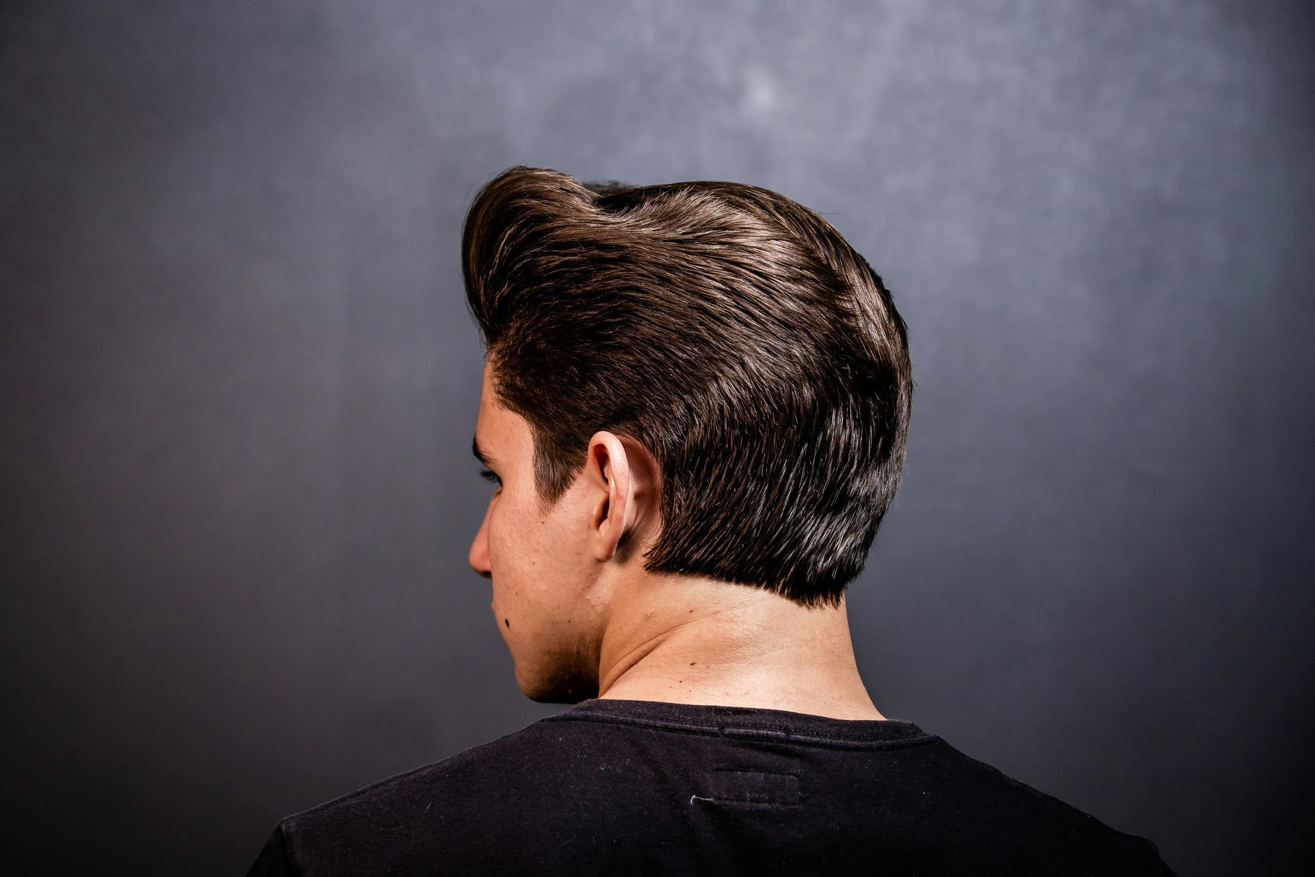 Man touching hairline, dark hair with signs of thinning and graying near the forehead.