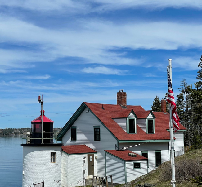 A lighthouse is sitting on top of a grassy hill next to a body of water.