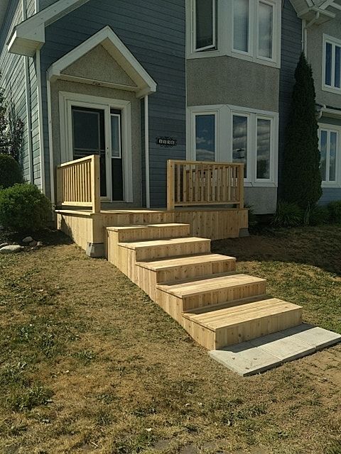 A newly built wooden deck with a set of stairs leading to the front door of a gray house with white trim.