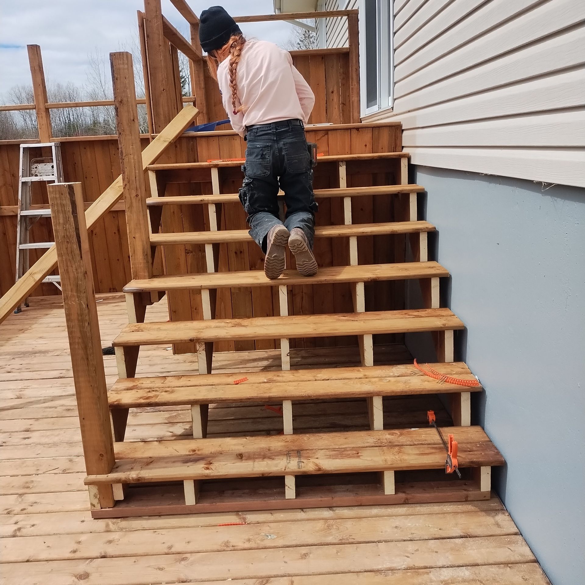 A person kneels on wooden stairs during construction of an outdoor deck.