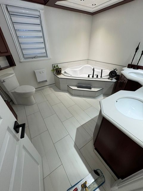 A modern bathroom with a white corner soaking tub, a toilet, a tiled floor, and dark wood vanity cabinets.
