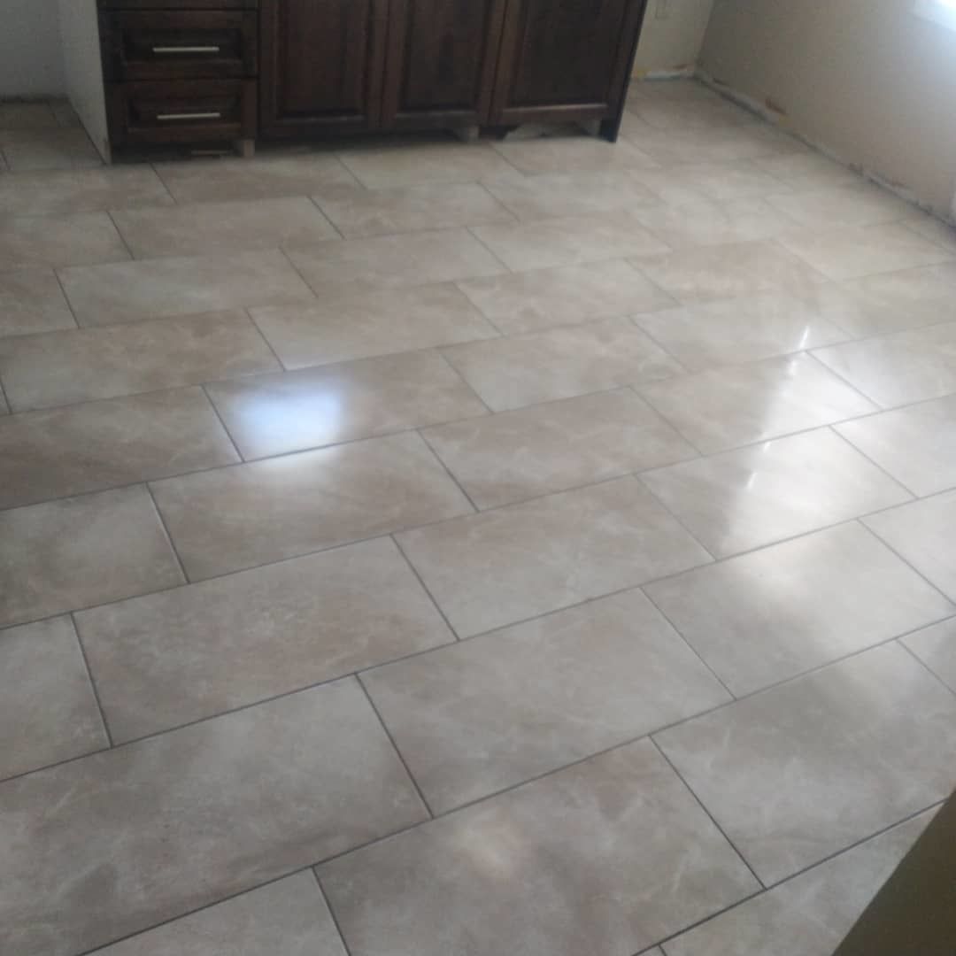 A room with large, rectangular, light-beige floor tiles arranged in a running bond pattern, next to a wooden cabinet.