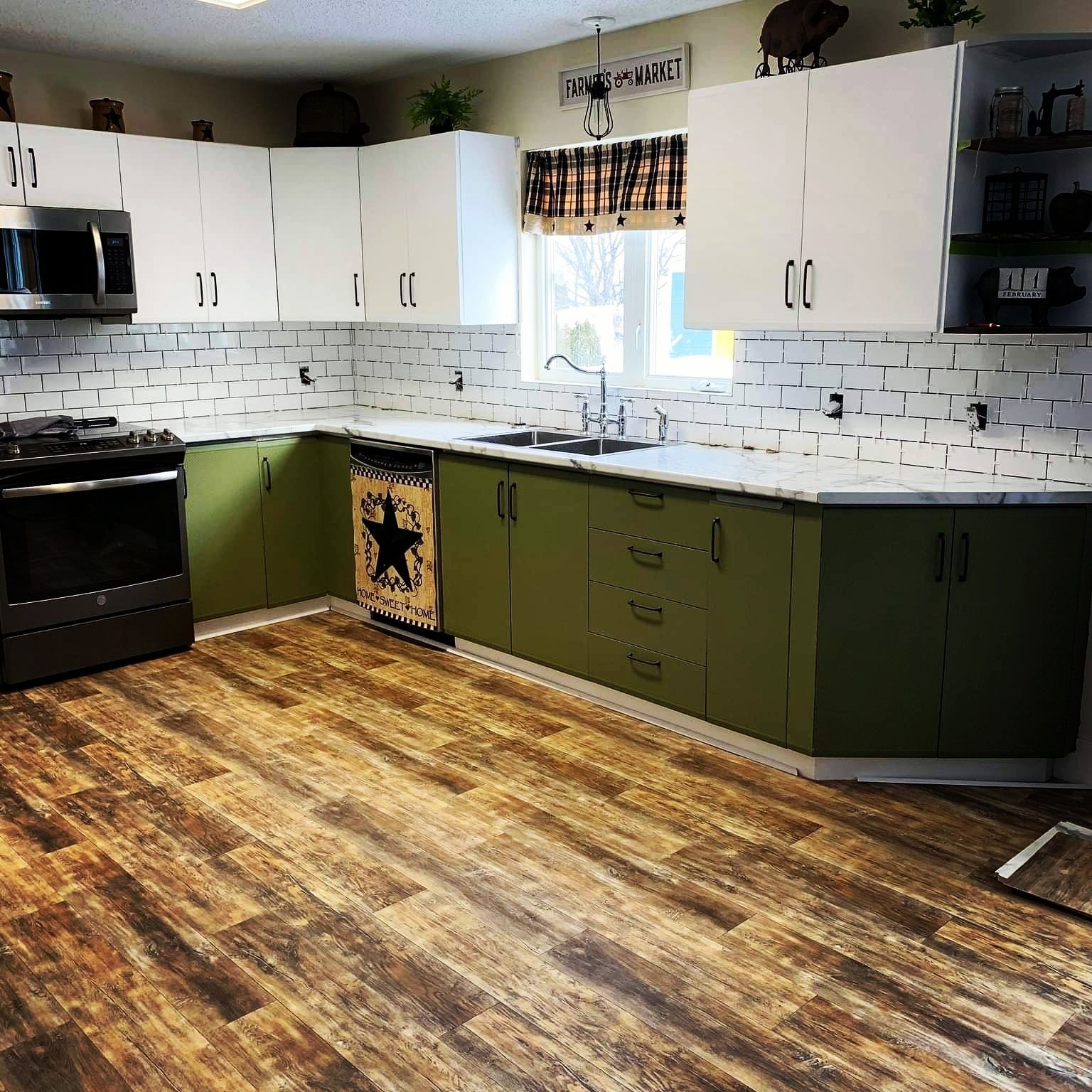 Kitchen with olive green lower cabinets, white upper cabinets, white faux-brick backsplash, and wood-pattern flooring.