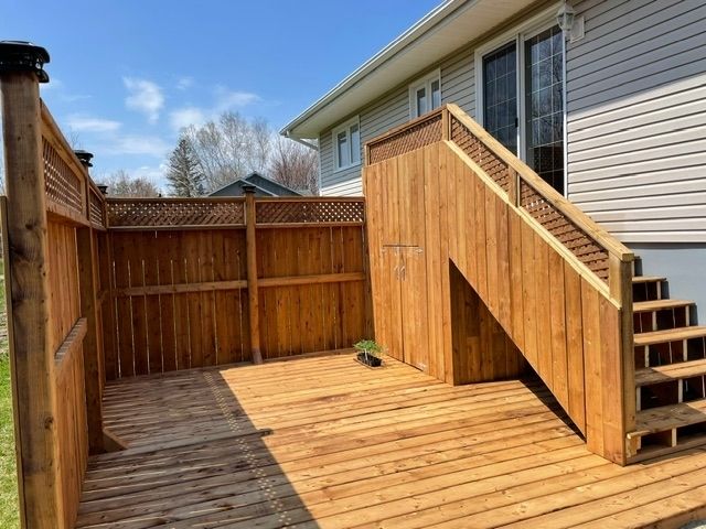 A wooden deck featuring a privacy fence, a built-in storage area under stairs, and light-colored house siding.
