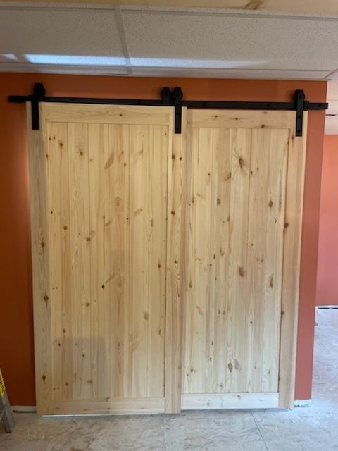 Two light-colored, unfinished wood barn doors with black metal sliding hardware on an orange wall.