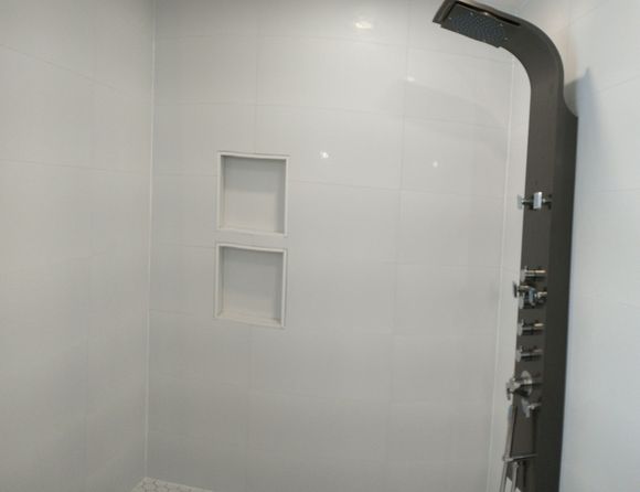 A modern shower stall featuring white tile walls, a built-in double-shelf niche, and a dark grey vertical shower panel.