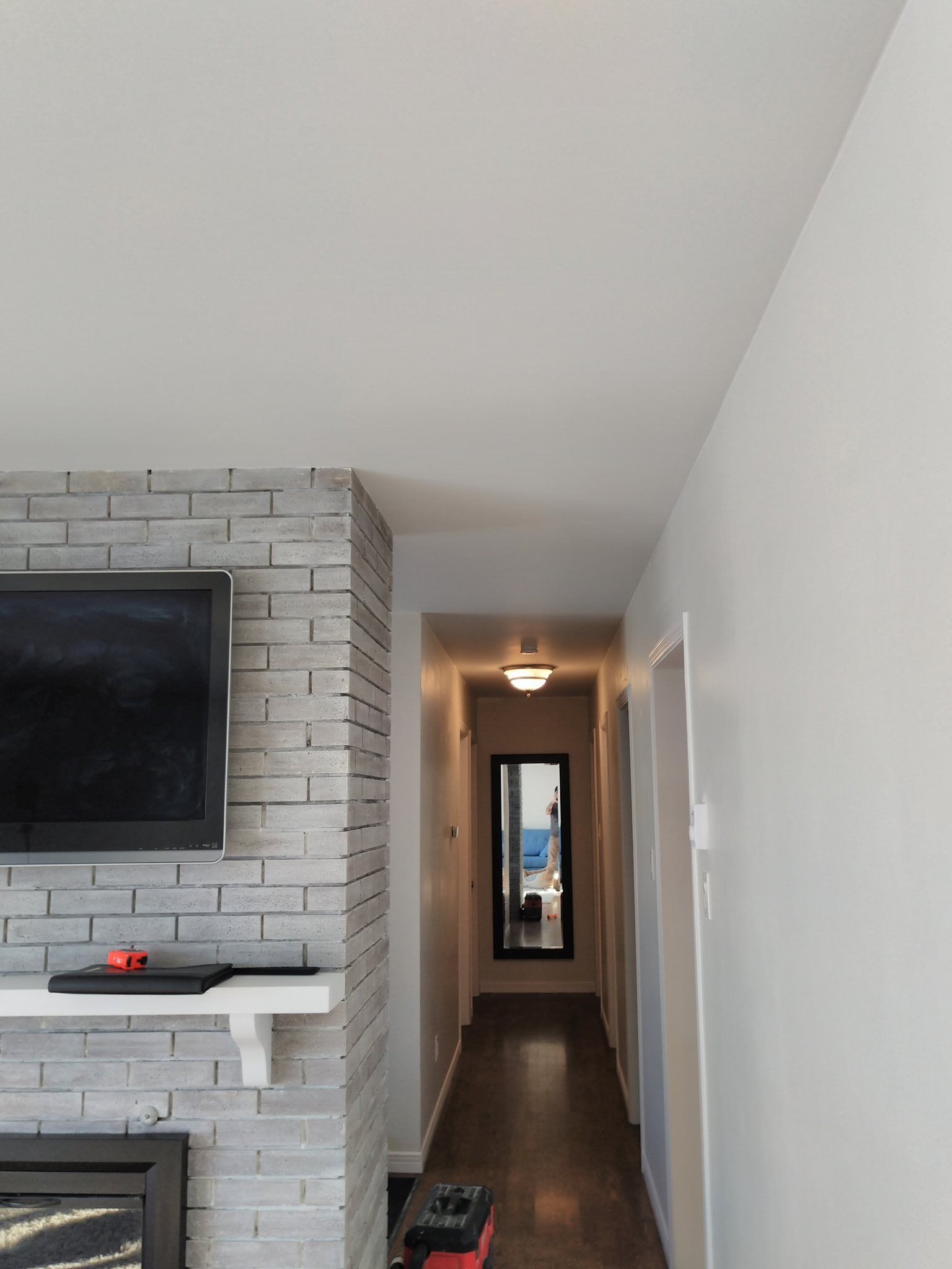 A view from a room looking down a hallway with a gray brick fireplace to the left and a mirror at the end of the hall.